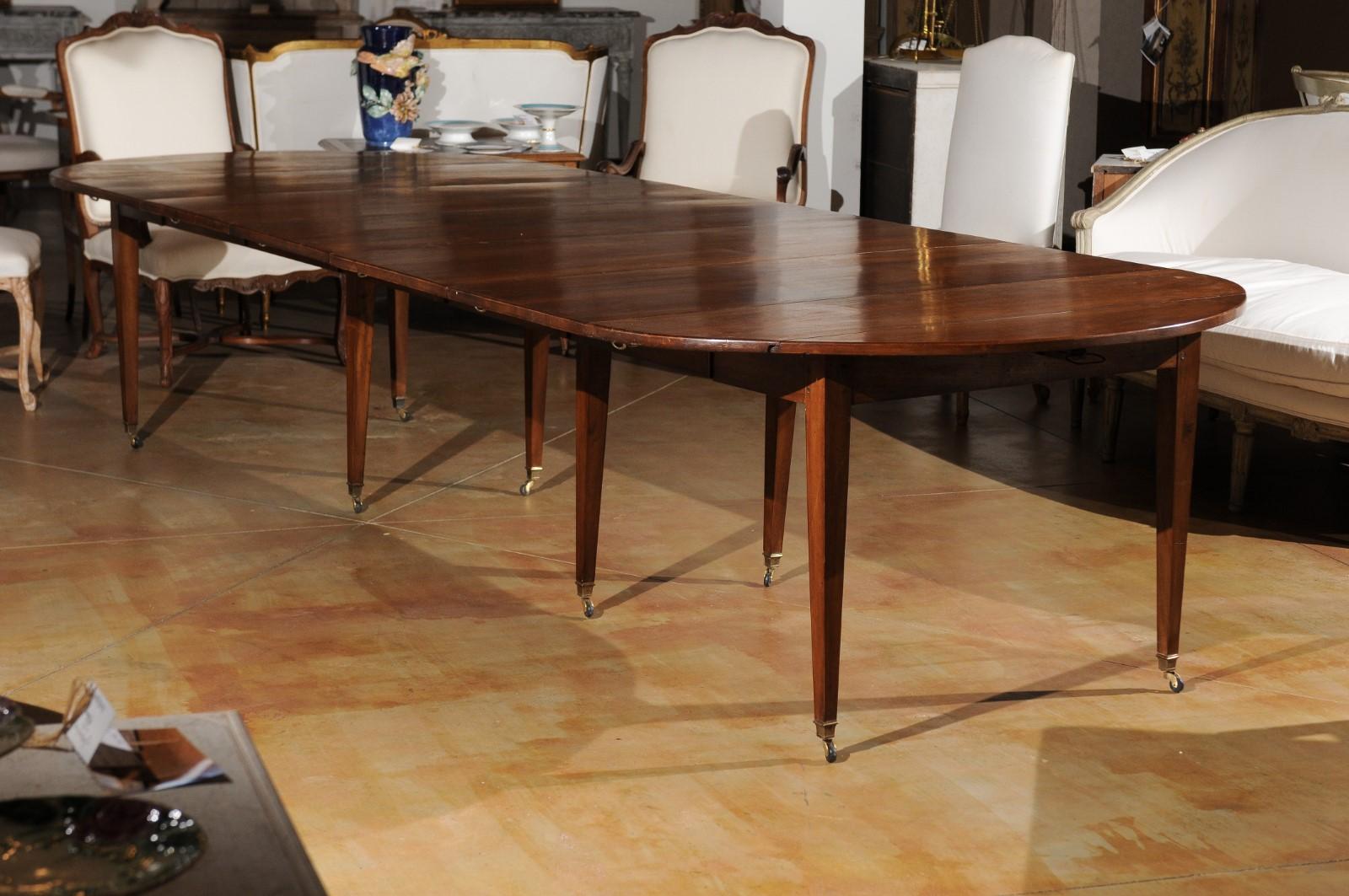 A French oval walnut extension dining room table from the 19th century, with drop leaves, tapered legs and casters. Born in France during the dynamic 19th century, this French dining room table features an exquisite walnut top presenting removable