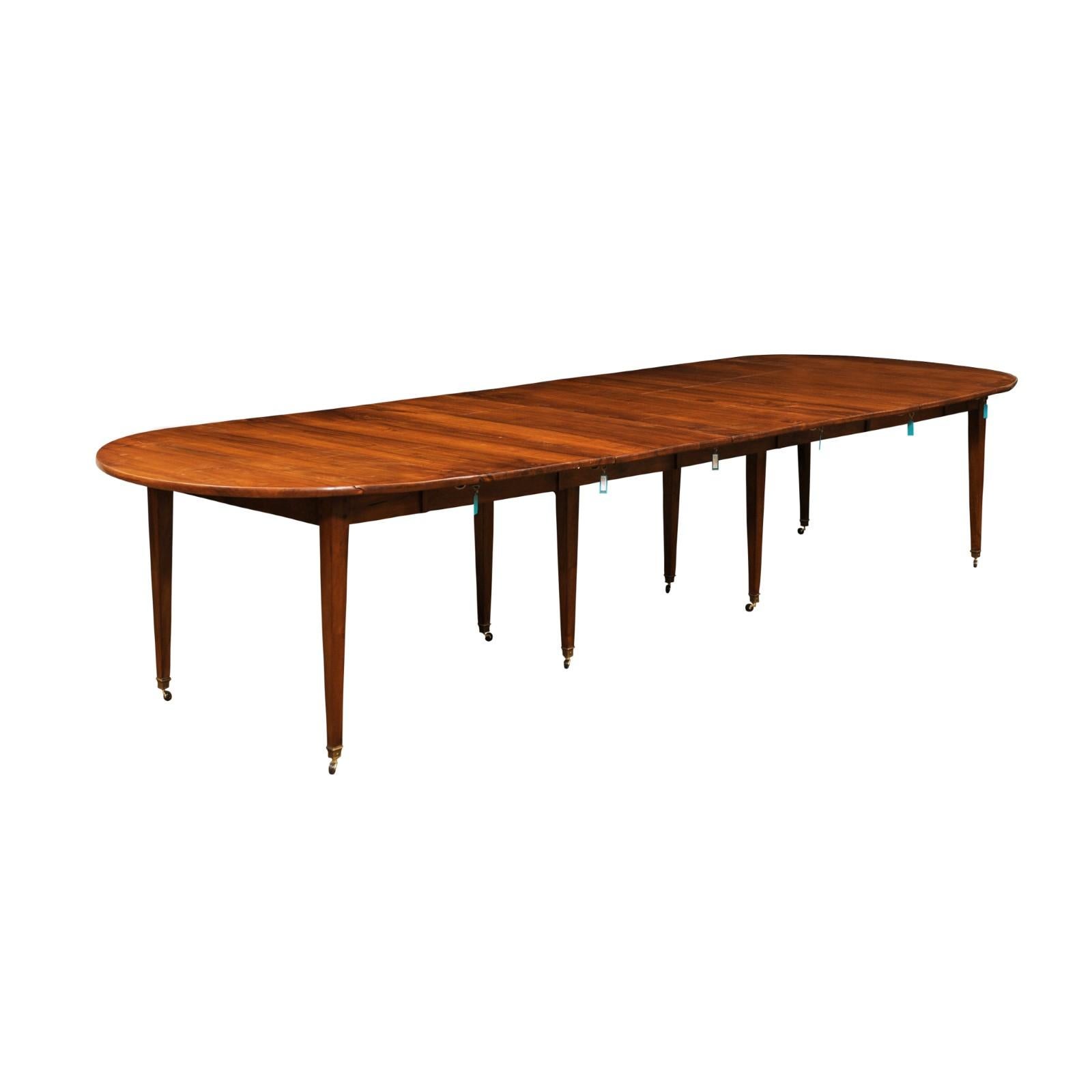 A French walnut oval extension dining room table from the 19th century, with five leaves, tapered legs and casters. Created in France during the 19th century, this French dining room table features a walnut oval top showcasing lateral drop leaves