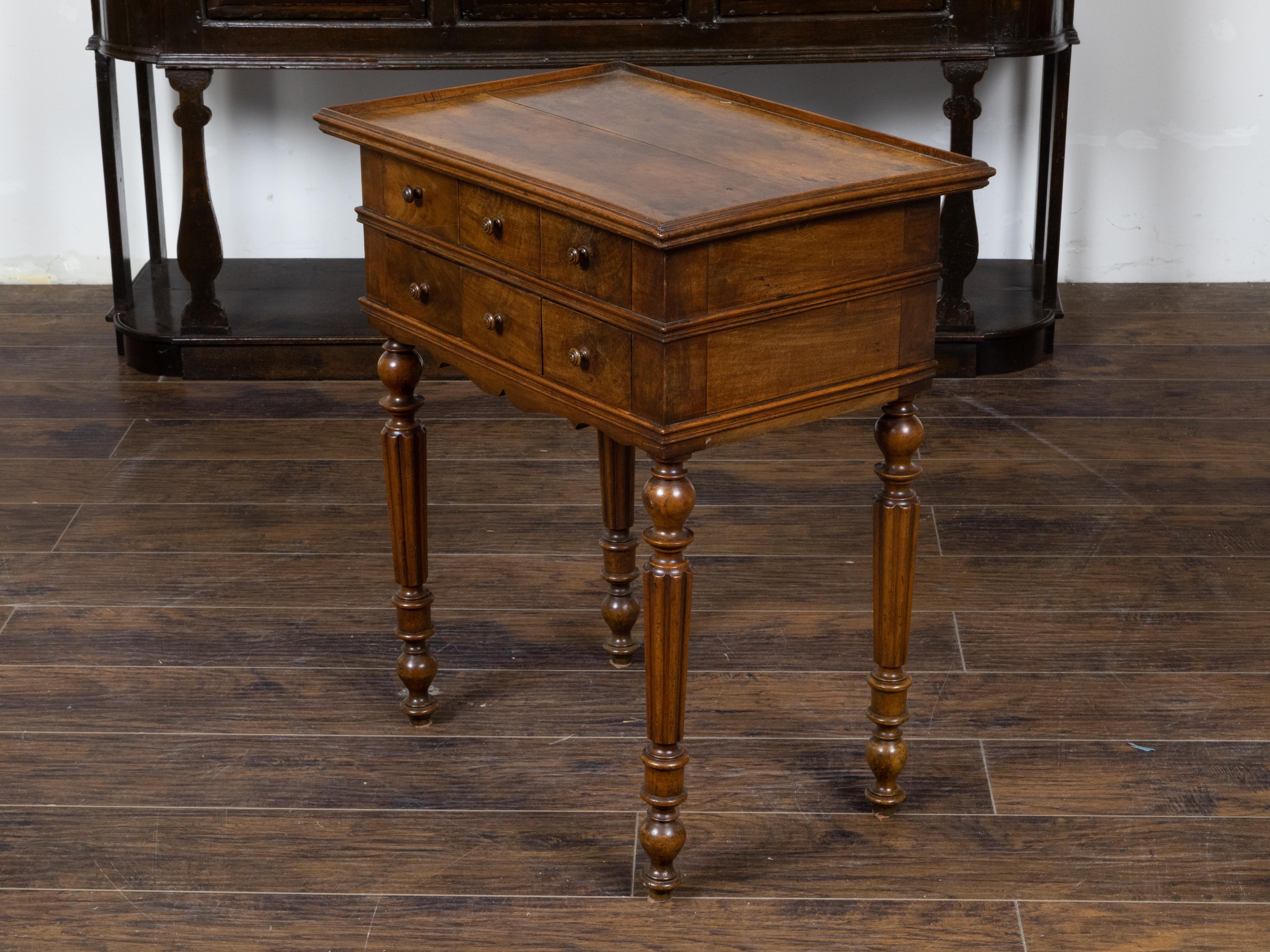 A French walnut side table from the 19th century, with tray top, six drawers, carved apron and four fluted legs. Created in France during the 19th century, this walnut side table features a rectangular planked tray top sitting above a perfectly