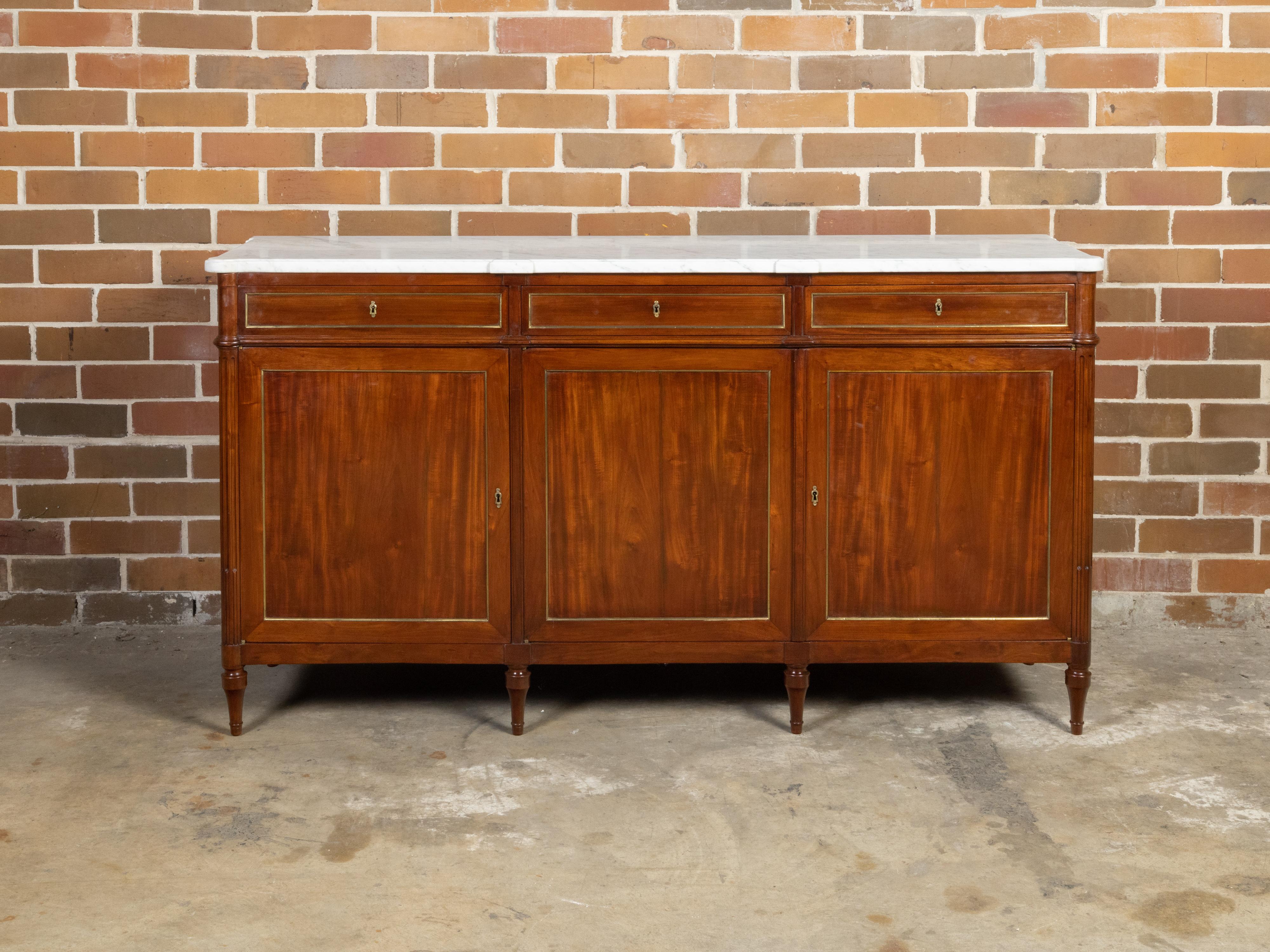 A French walnut sideboard from the 19th century with white marble top and three drawers over three doors. Created in France during the 19th century, this walnut sideboard features a rectangular white marble top with protruding accents and rounded