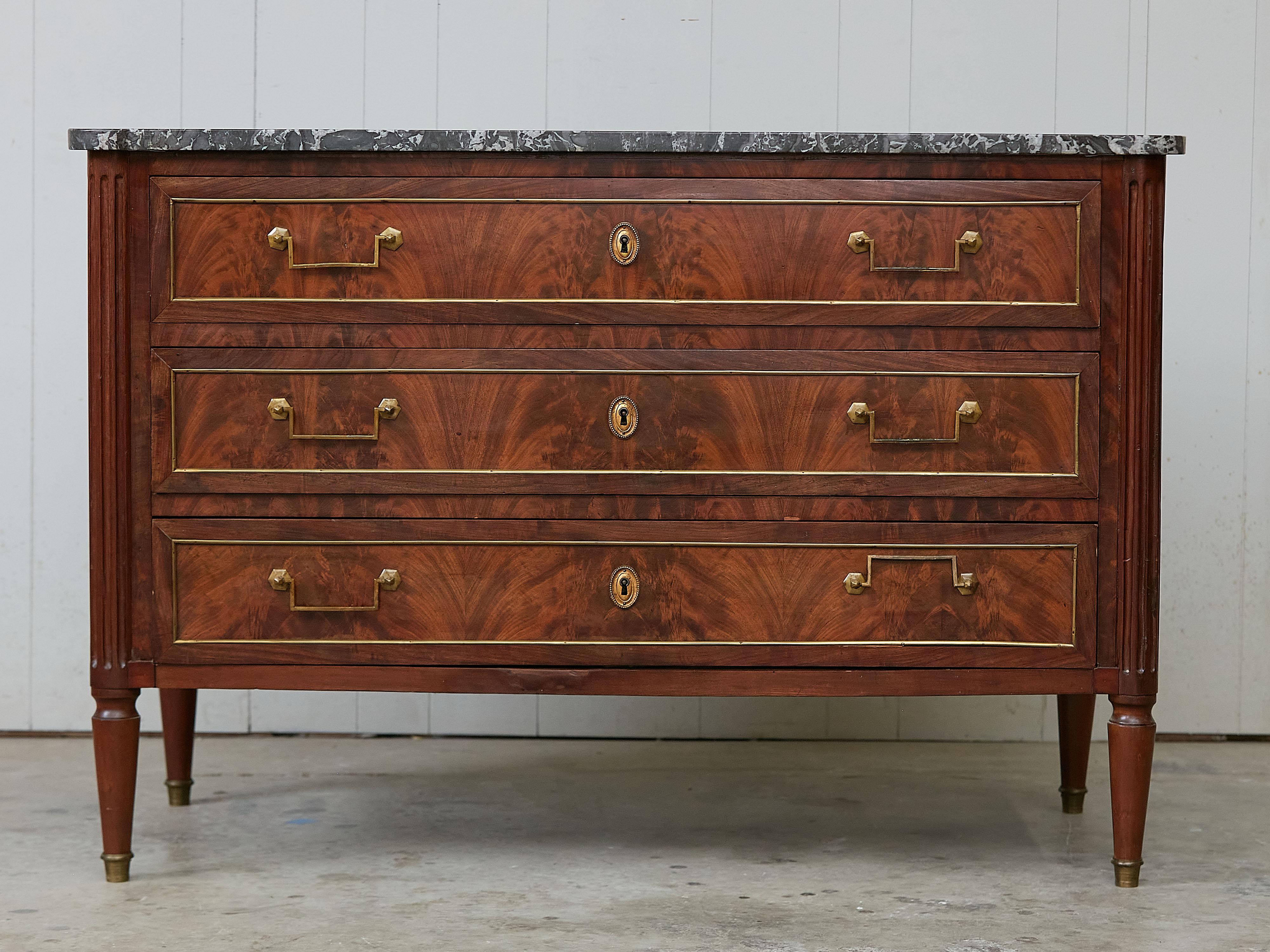 A French walnut commode from the 19th century, with butterfly veneer and grey marble top. Created in France during the 19th century, this walnut commode features a grey veined marble top with rounded corners in the front, sitting above three drawers