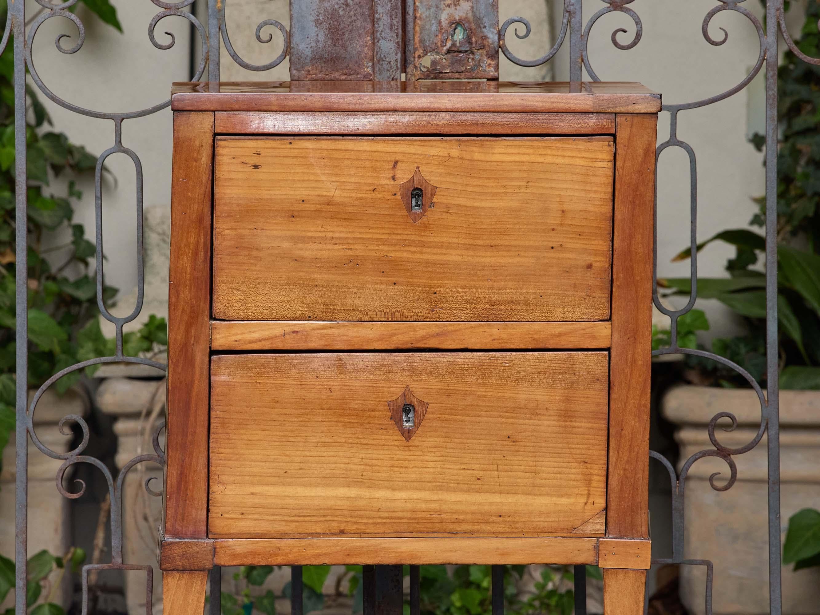 A French walnut side table from the 19th century, distinguished by its clean lines and warm patina. Rectangular in form, the table features two full-width drawers, each fitted with a small shield-shaped escutcheon surrounding the keyhole. The