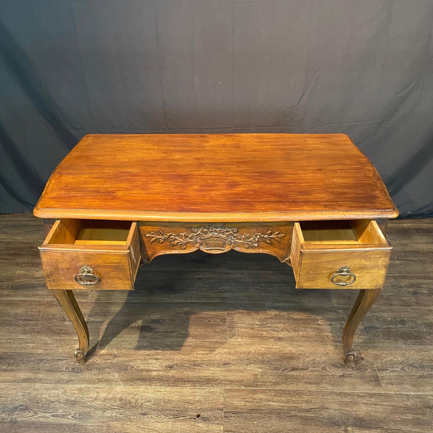 Classic provincial French writing desk from the 19th century that could also serve as a beautiful walnut side table, dressing table / vanity or console . Note the intricately carved center apron urn with floral adornment on both the front and back!