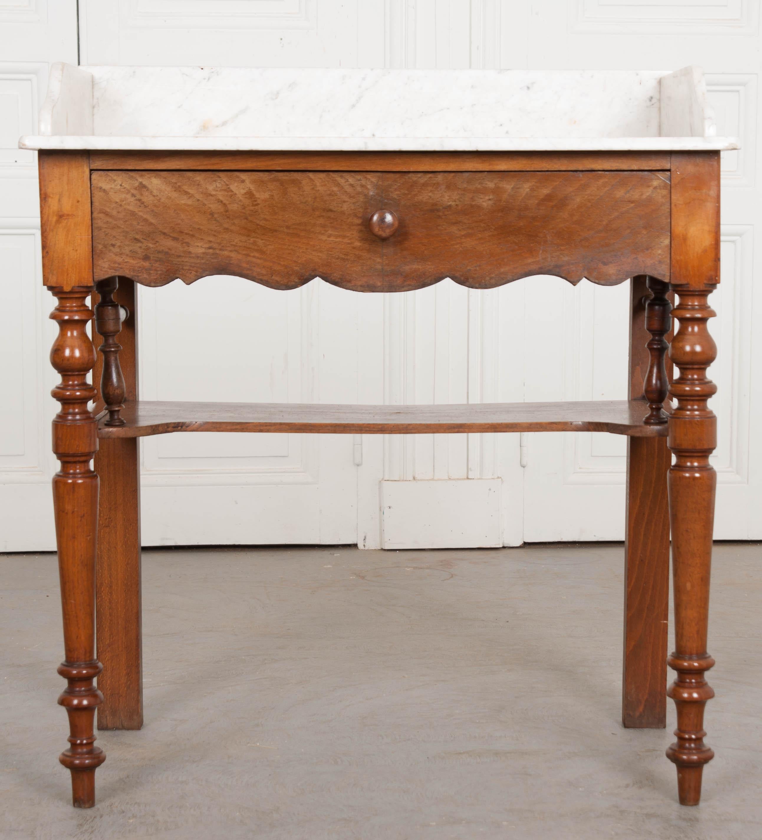 French washstand with marble top, circa late 1800s, is made of walnut and is accompanied with one large drawer and two-fold-out towel holders. It is supported by turned carved legs linked equally with a substantial shelf-stretcher. The marble top is