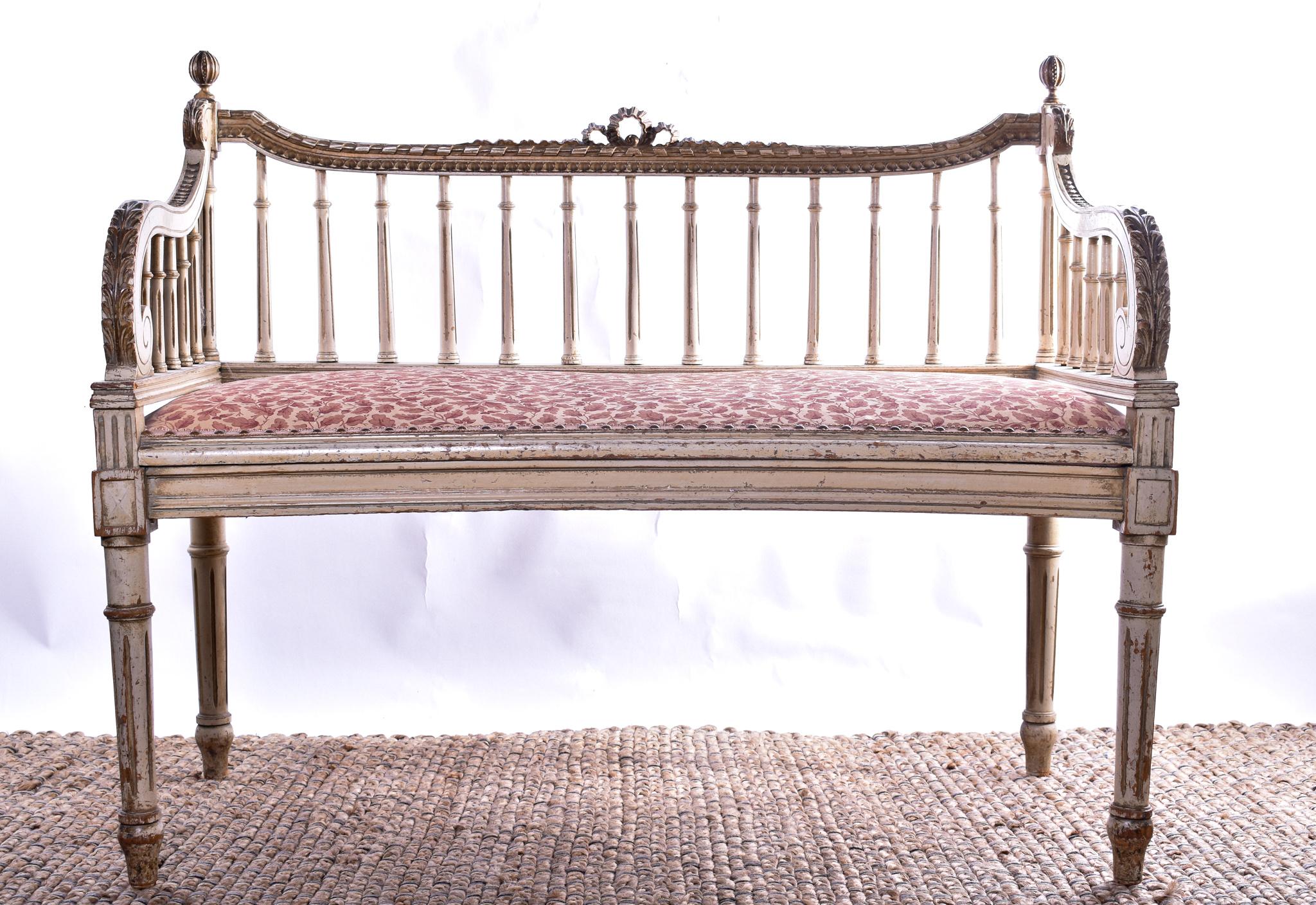 A very smart white-painted window seat, French late 19th century. The shaped top rail with a ribbon crest over a spindle back and sides, the seat originally caned has been upholstered in red and cream fabric decorated with in keeping oak