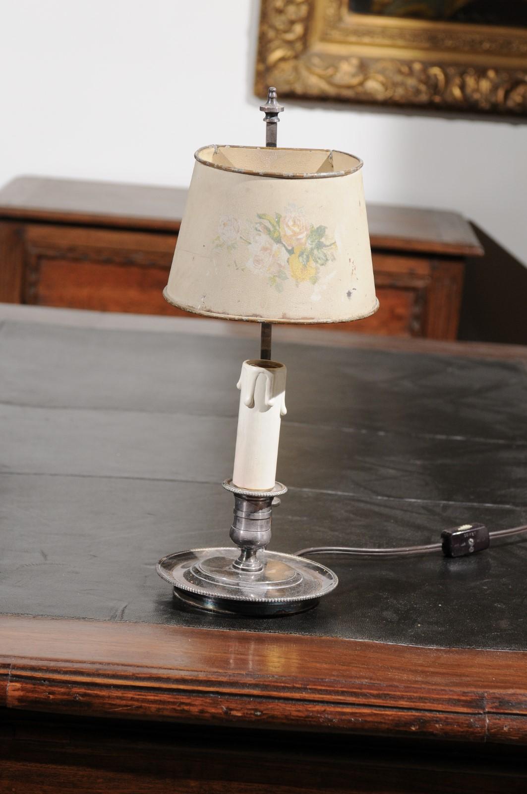 A French tôle lamp from the 19th century, with original hand painted shade. Born in France during the 19th century, this charming tôle lamp is adorned with a ring in the back that allowed the item to be moved at will. The lamp is resting on a