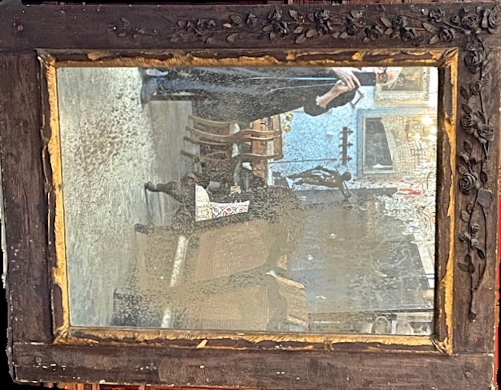 This is an example of an early 19th Century wall mirror. The frame has a hand carved roses swag into the left side and on the top of the frame. The mirror glass is the original and is partly faded. It can be hung either way.