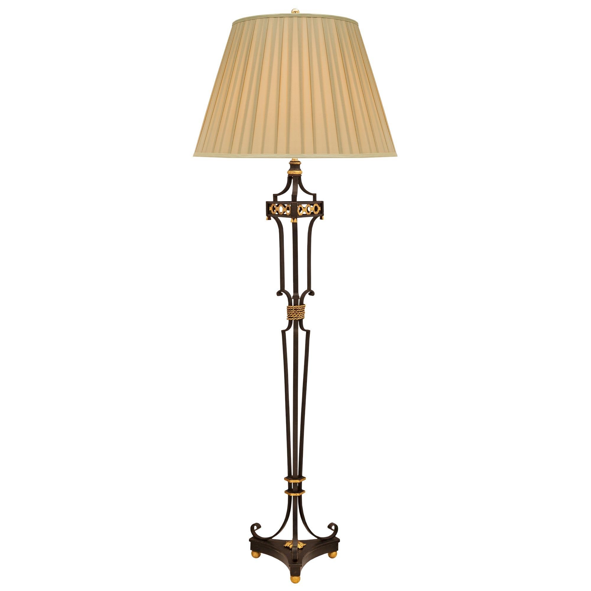 Un élégant et très décoratif lampadaire français du 19ème siècle en fer forgé et métal doré. Le lampadaire est surélevé par une base triangulaire aux angles coupés, aux côtés concaves et à trois pieds à boule en métal doré fin. Trois magnifiques