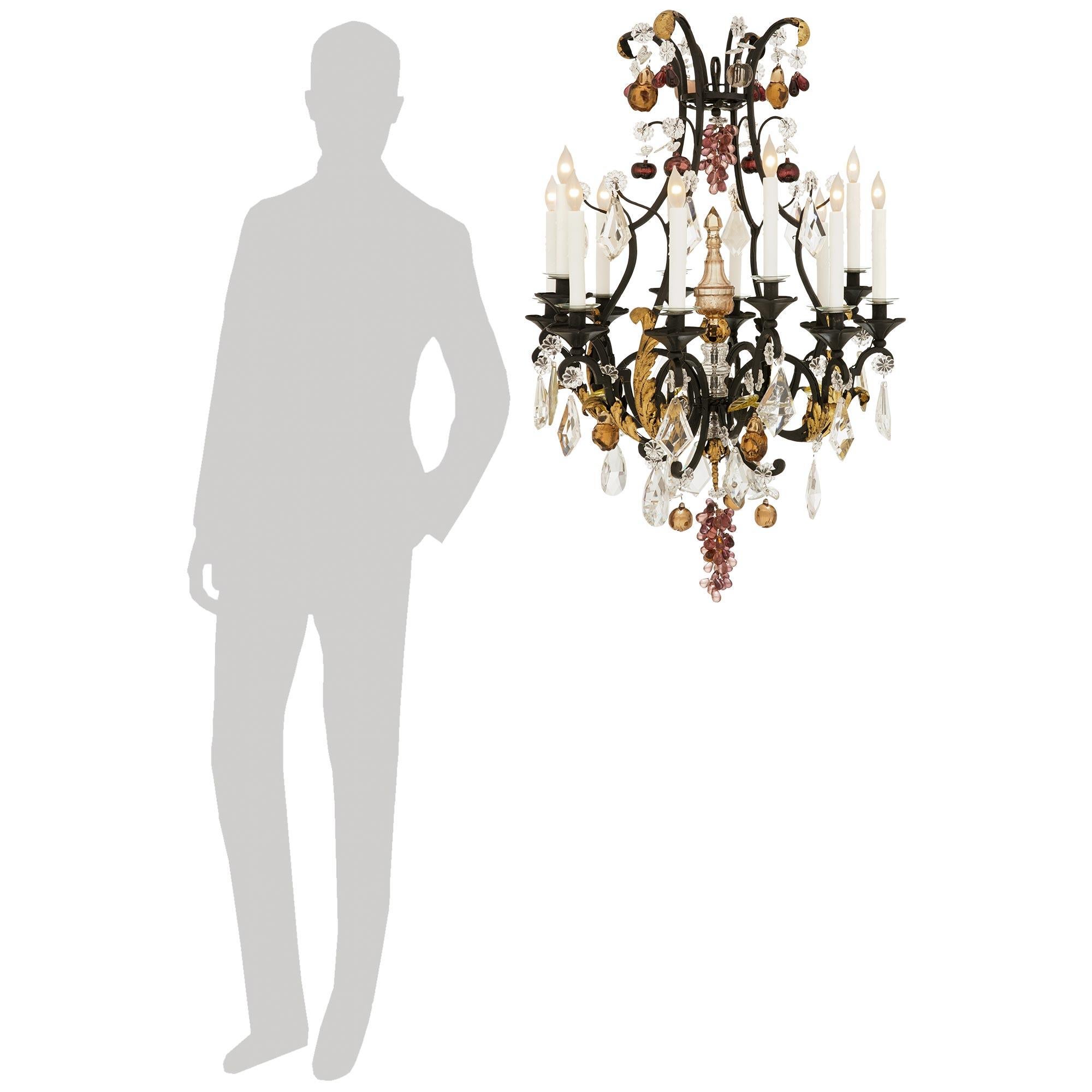 Un bellissimo e decoratissimo lampadario francese del XIX secolo in ferro battuto, dorato e con cristalli Baccarat. Questo splendido lampadario a dodici bracci e dodici luci è centrato, nella parte inferiore della gabbia a volute, da un grazioso