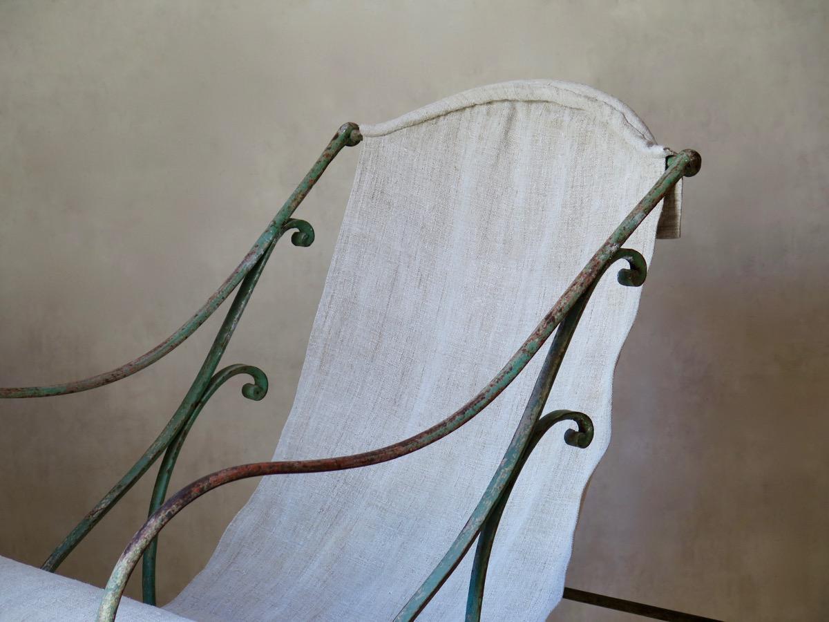 Wonderful, sturdy wrought iron rocking chair of generous proportions. The iron retains most of its original green paint, and is delicately adorned with curlicued details. Upholstered in heavy, natural-colored, antique linen. Possibly from Arras.