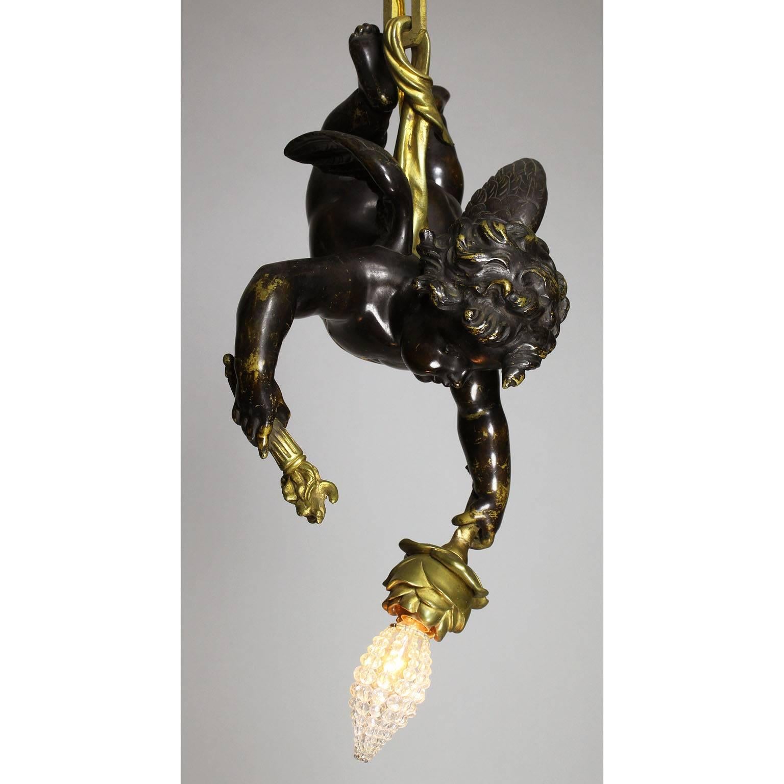 A fine French 19th-20th century Belle Époque patinated and gilt bronze single-light figural cherub chandelier pendant. The hovering patinated bronze cherub suspended by a gilt-bronze strap wrapped around his belly, holding a single-flame-torch and a