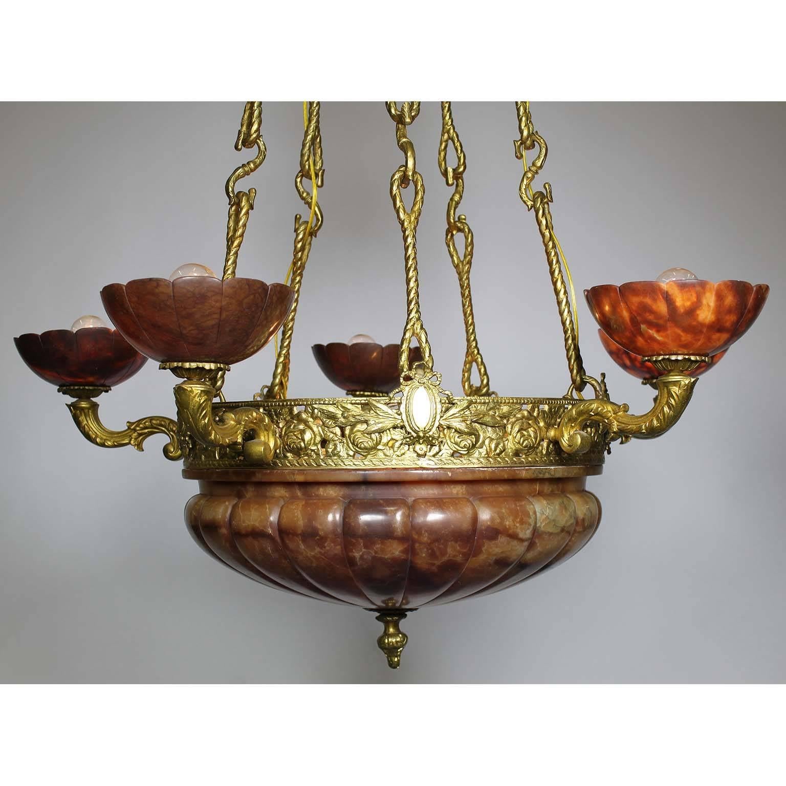 Lampadario a cinque luci in bronzo e alabastro rubino intagliato, Francia, inizio XX secolo. La struttura in bronzo traforato, sospesa da cinque sostegni in bronzo a forma di corda e sormontata da cinque luci a forma di voluta, tutte dotate di