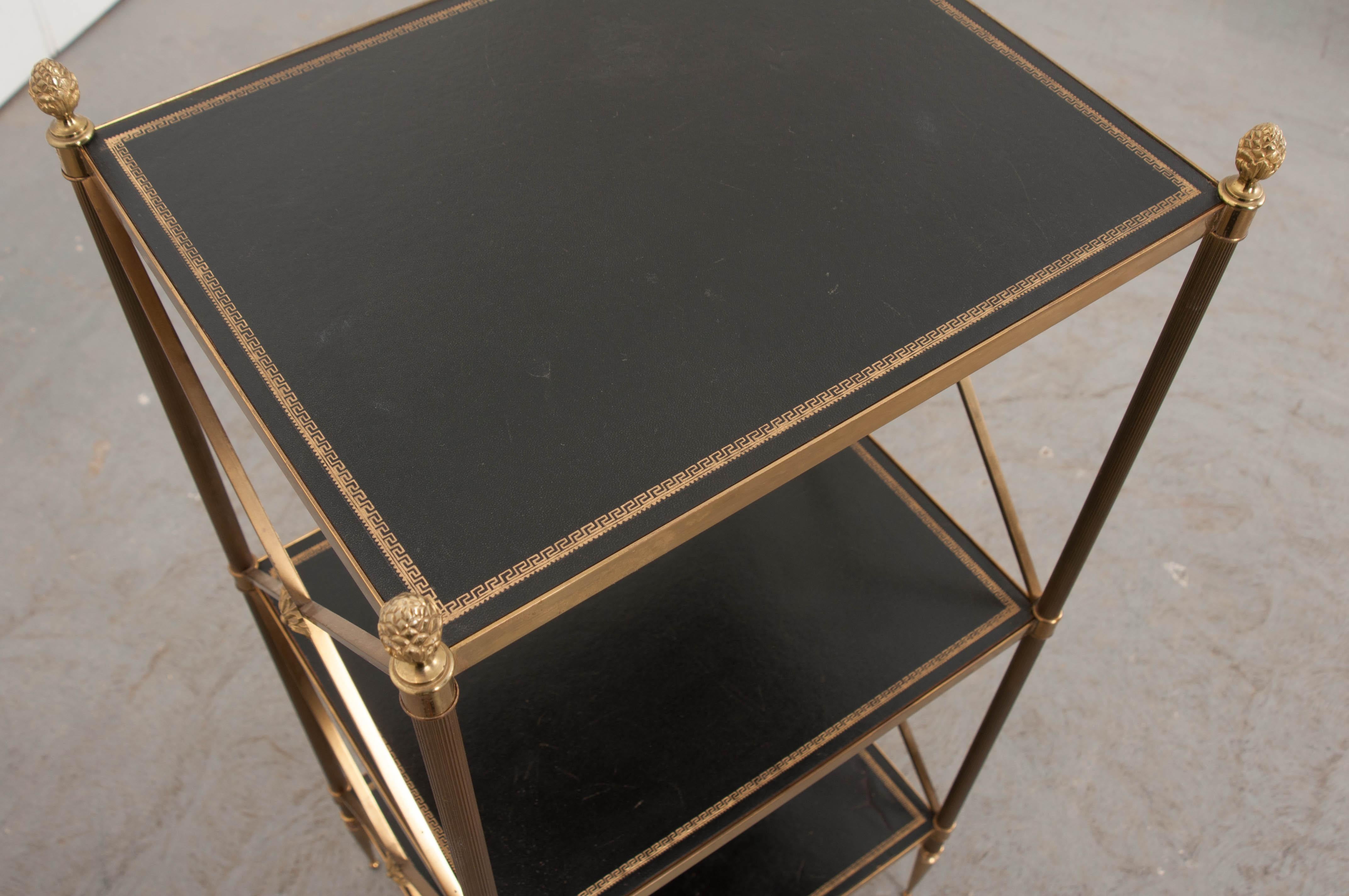 This stylish brass and leather étagère in the Neoclassical taste is from 1920s France and has two shelves lined in brown leather separated by a brass frame with acorn finials, x-form supports and arrow feet.