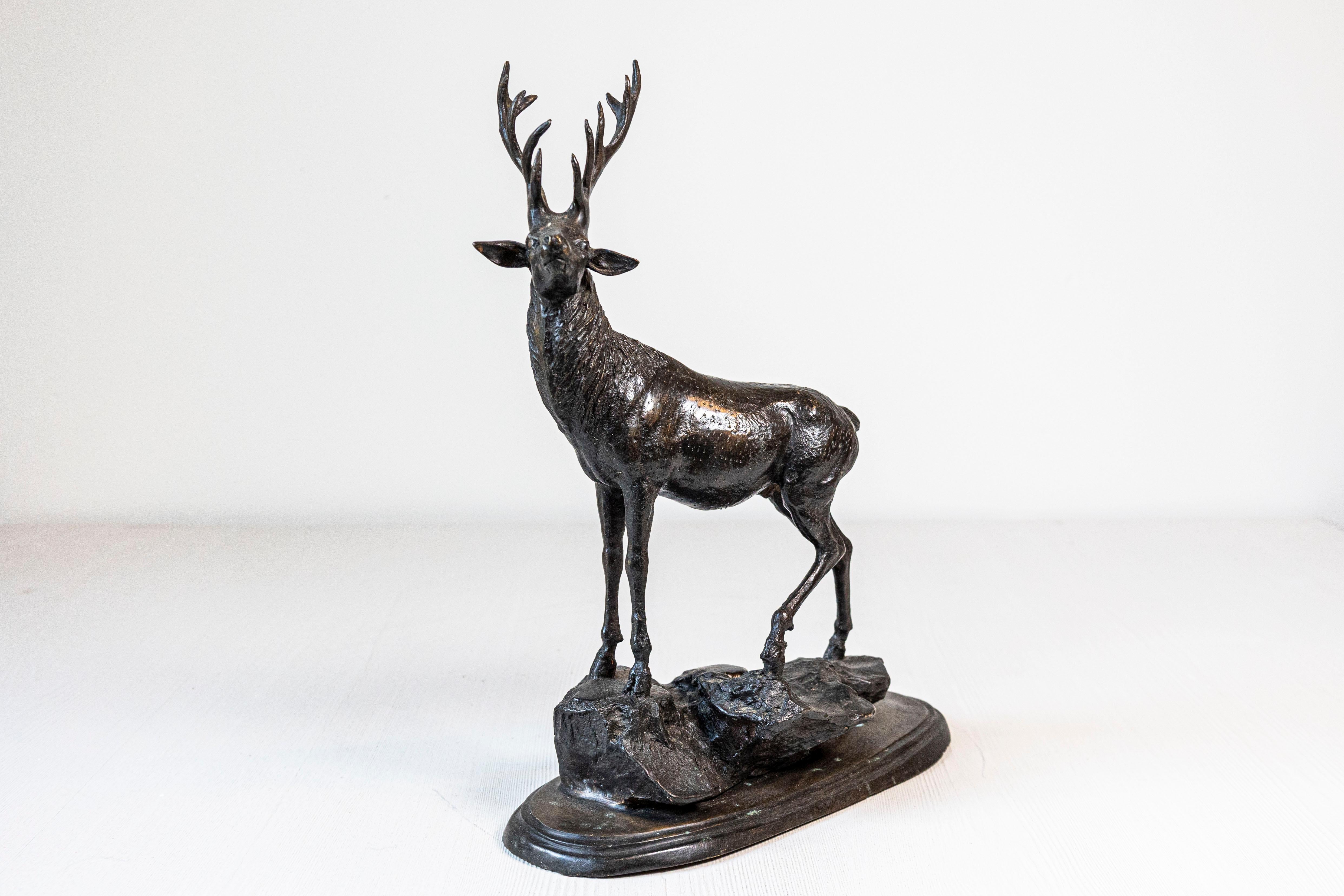 This French 20th-century bronze statue, dating to circa 1920, depicts a majestic deer standing proudly on a textured, naturalistic base. The sculpture is crafted from bronze using the lost-wax casting technique, which allowed artisans to achieve