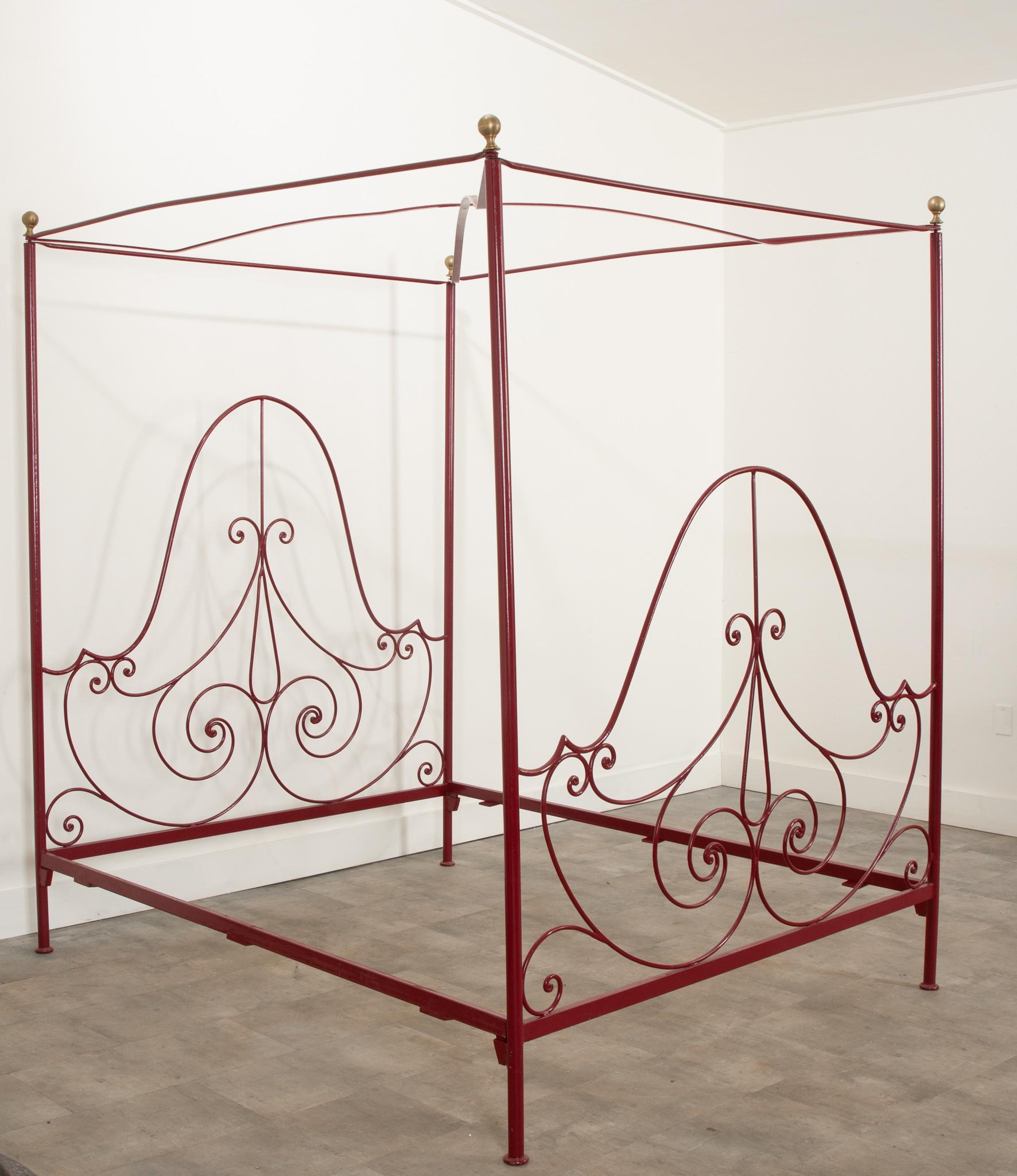 We just adore this canopy bed from 20th Century France. It's powder coated in a rich pomegranate shade and is in great vintage condition. Its canopy top is secured under brass spherical finials. Gorgeous S and C scrolls come together to compose the