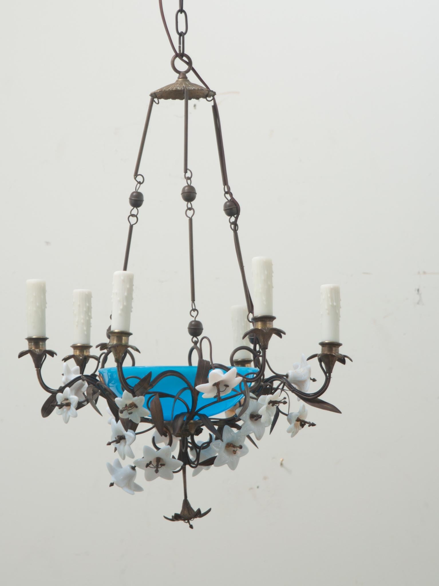 A vintage 7-light floral chandelier made in France. The fixture, most likely found in a church, has a bright blue opaline glass dish with a bulb inside and is surrounded by milk glass and bronze flowers, and has six curving arms with faux candle