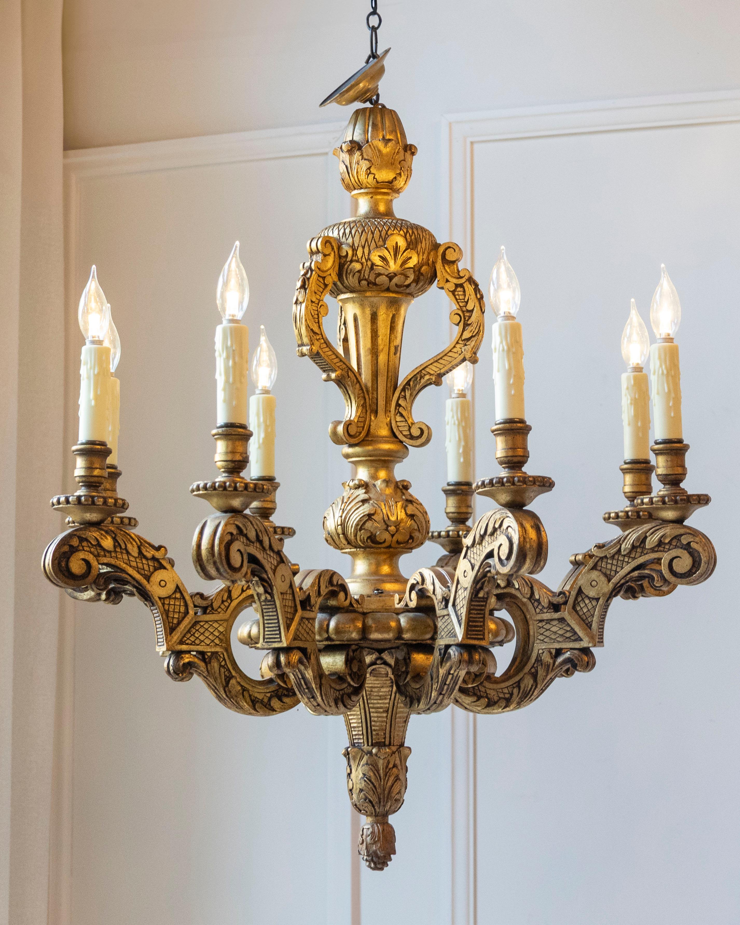 Questo straordinario lampadario in legno dorato francese del XX secolo è un raffinato esempio di illuminazione scultorea che unisce l'esuberanza barocca all'eleganza senza tempo. La cornice in legno intagliato è riccamente ornata da foglie d'acanto