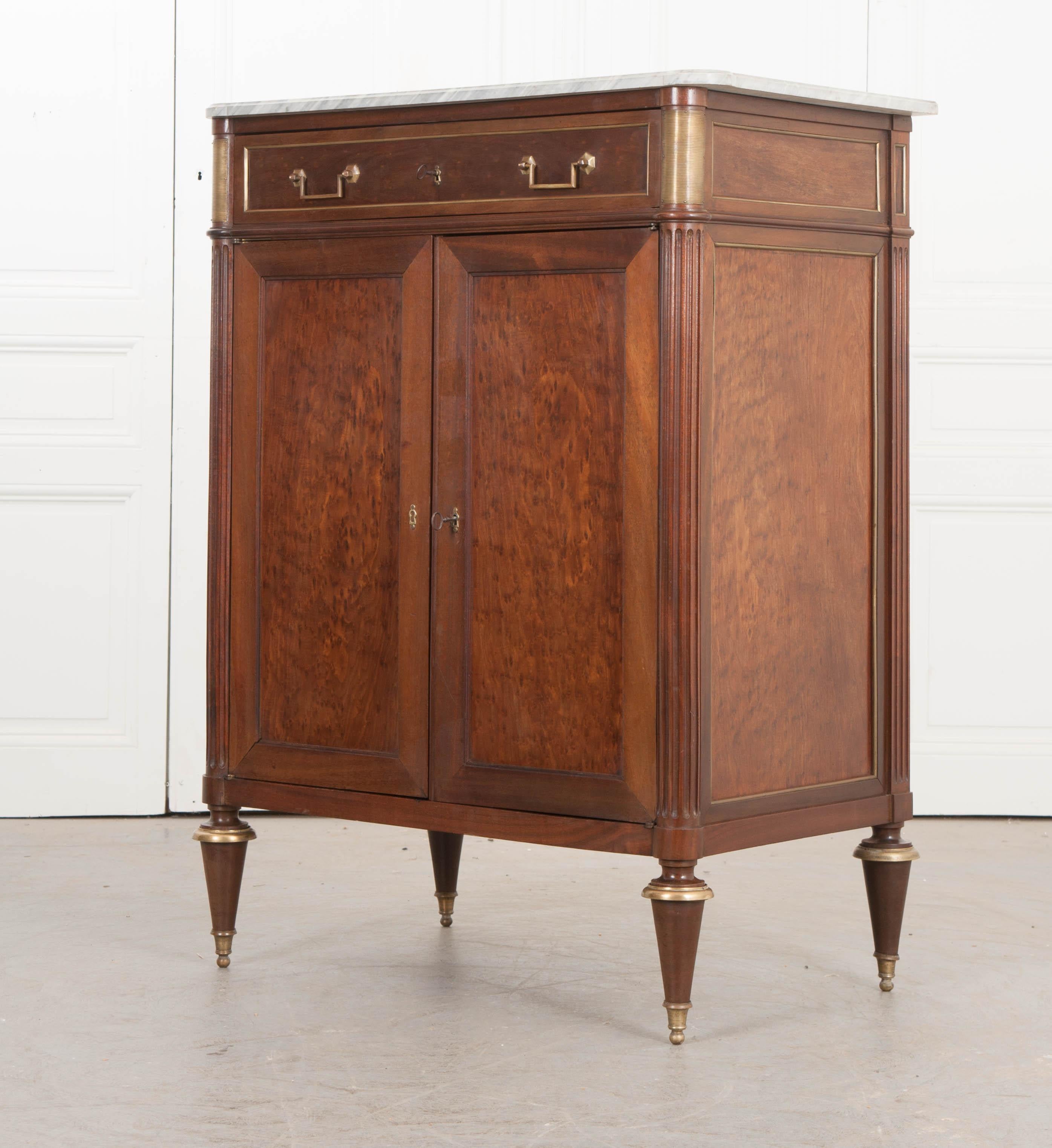 This lovely French Louis XVI-style marble-top bird’s-eye mahogany tall cabinet, circa 1940s, from France, has a beautiful pale-grey and white marble top with turreted corners, over a conforming case with a single paneled long apron drawer trimmed in