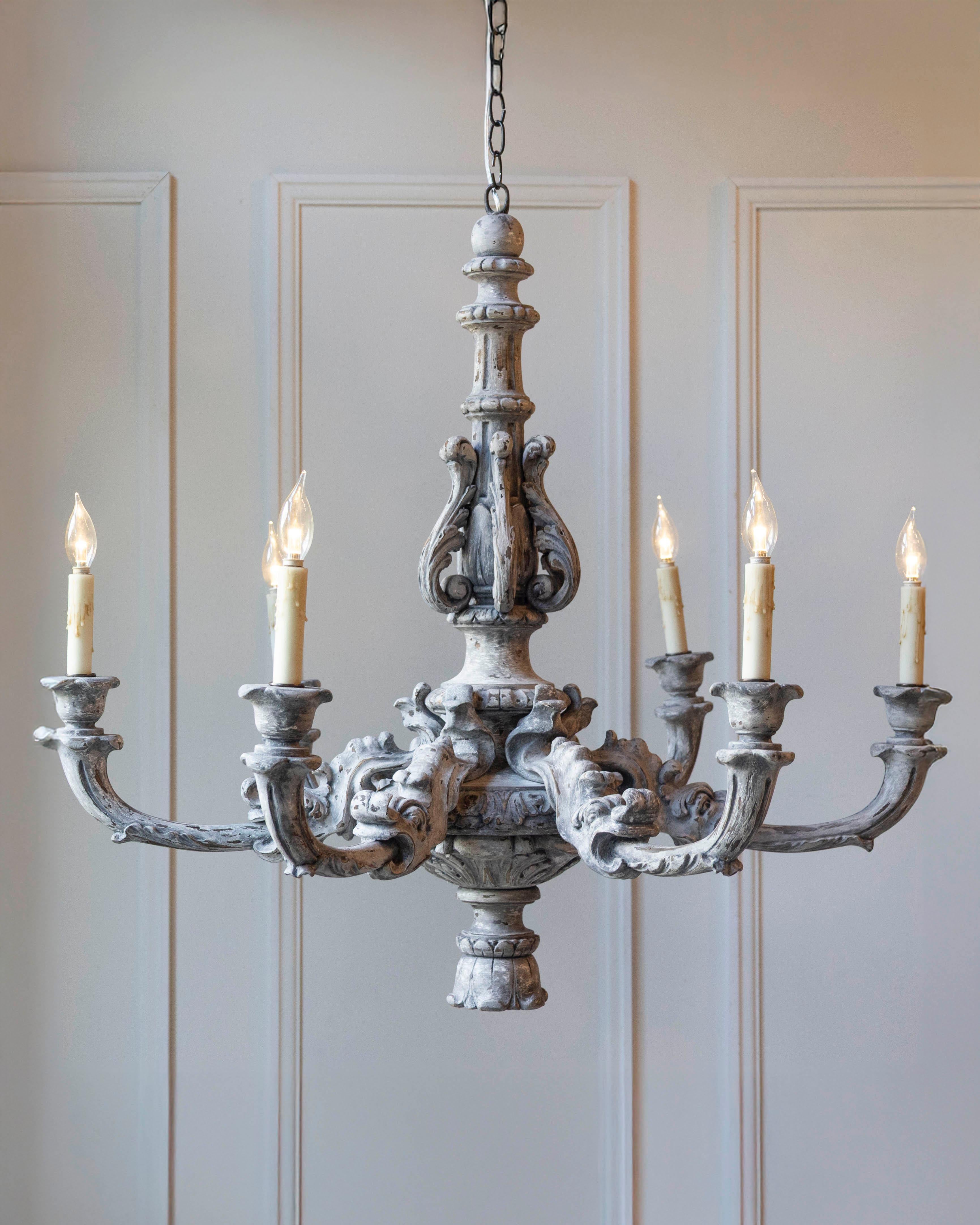 Un raffinato lampadario francese in legno intagliato del XX secolo, elegantemente realizzato a mano con una ricca decorazione a volute e ornamenti classici. I sei bracci graziosamente arcuati del lampadario si estendono da un robusto balaustro