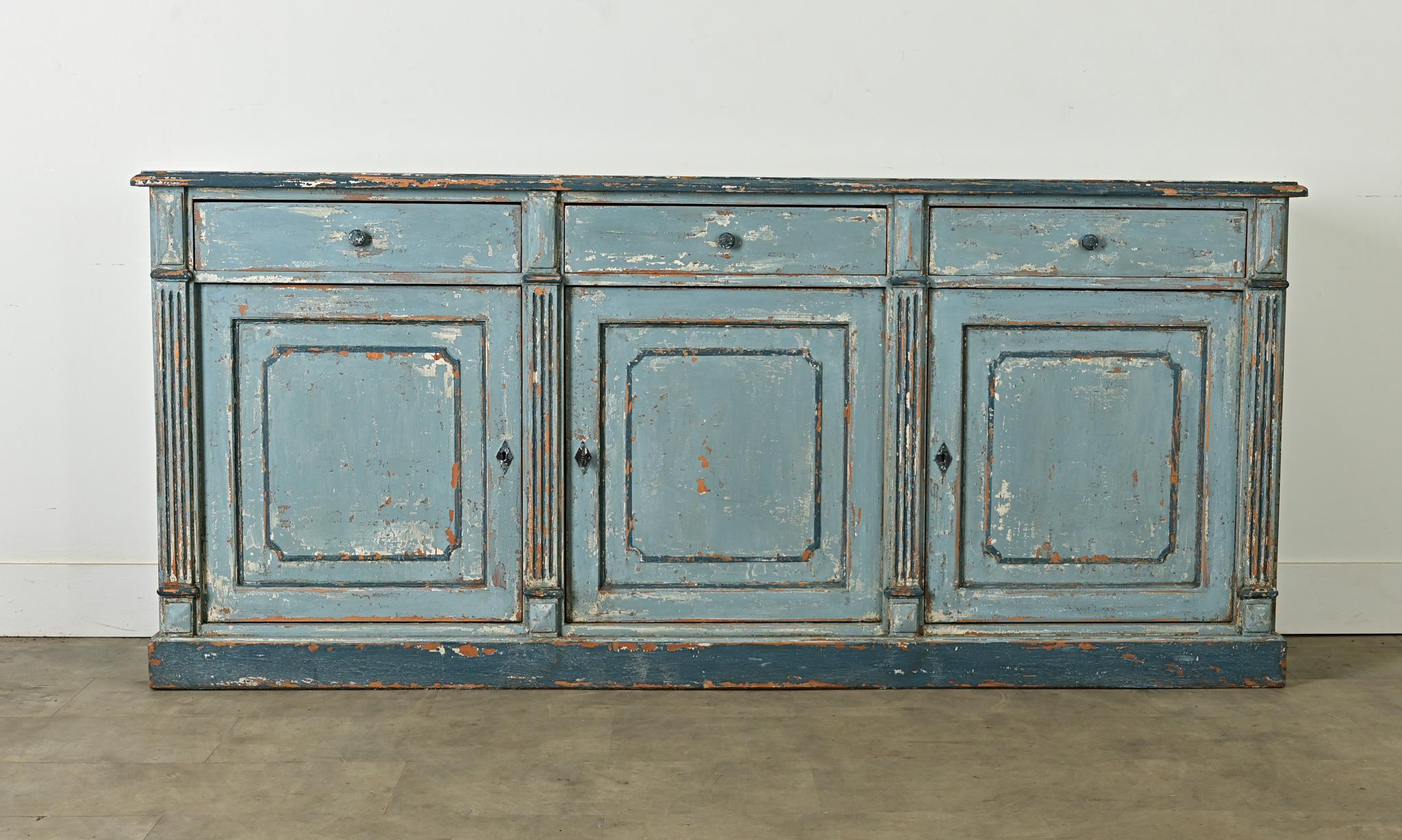 A 20th century transitional enfilade, influenced by the visual codes of Louis XVI and Gustavian painted furniture, this buffet–or sideboard–can work in many interior styles. The soothing blue color is charmingly patinated to reveal the pine wood