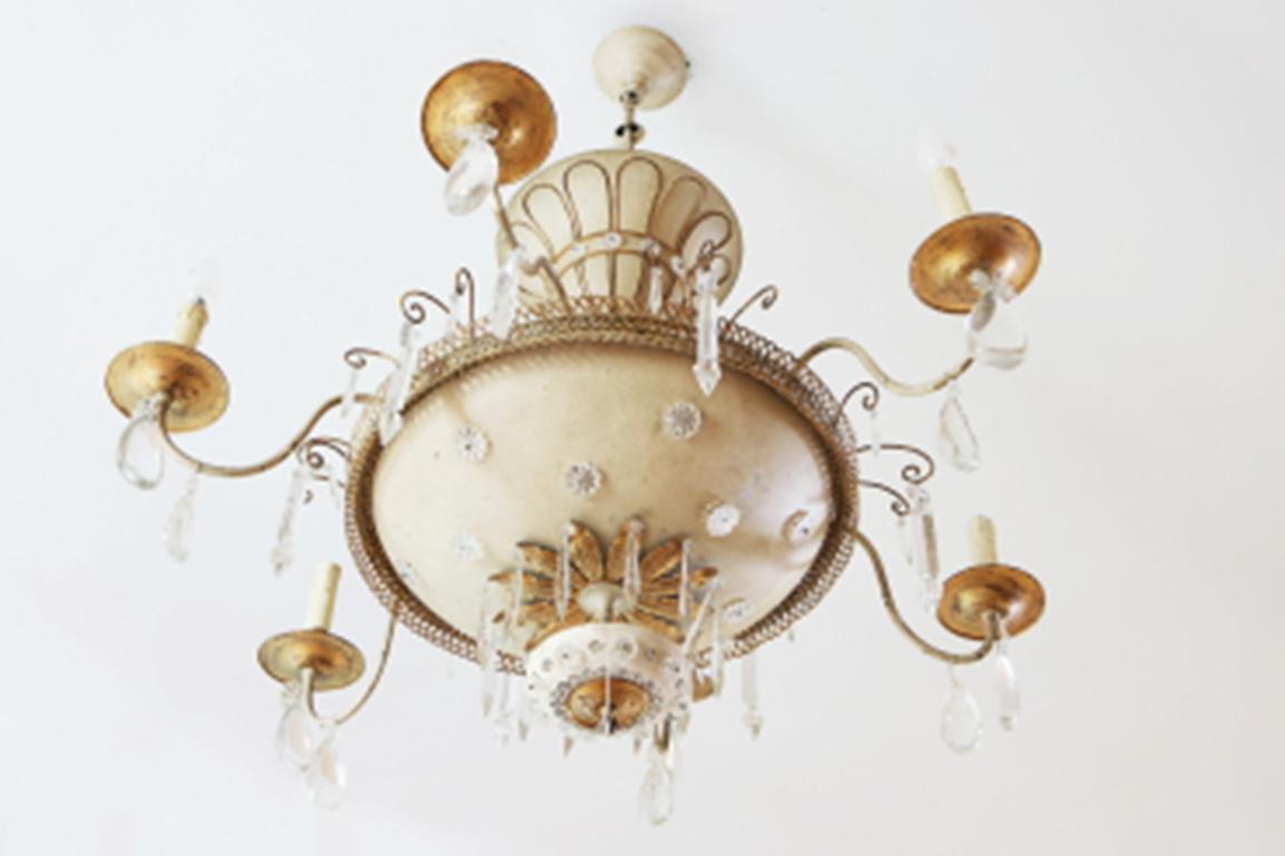 A French 20th century parcel-gilt and cream white painted Maison Baguès six-light chandelier. Decorated with faceted glass drops, pendants and flowerheads overall. A central dish issuing six 