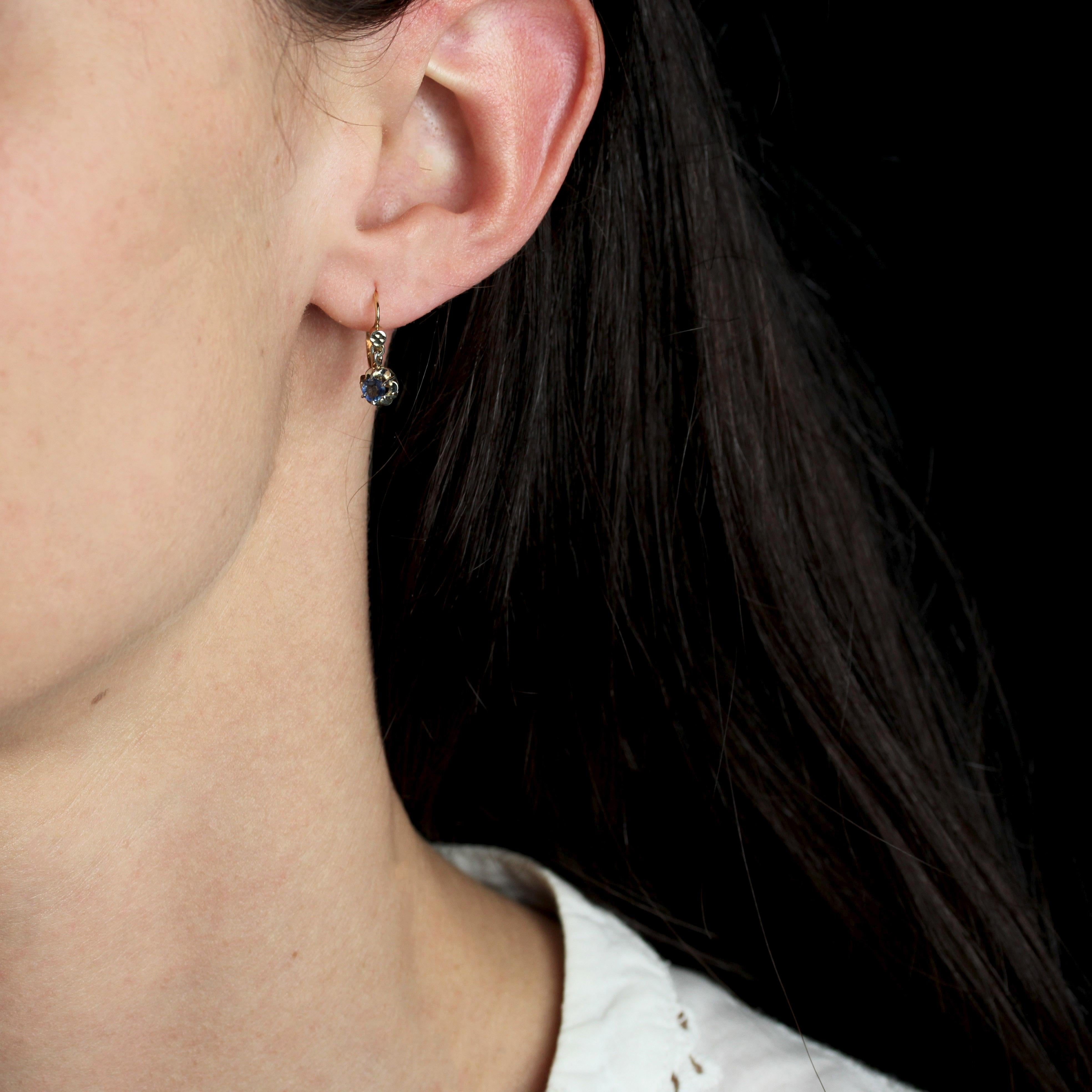 For pierced ears.
Earrings in 18 karat yellow gold, eagle head hallmark.
Charming antique earrings, each adorned on the front with a round sapphire, held in place with claws and topped by a small flower motif. The clasp threads through the