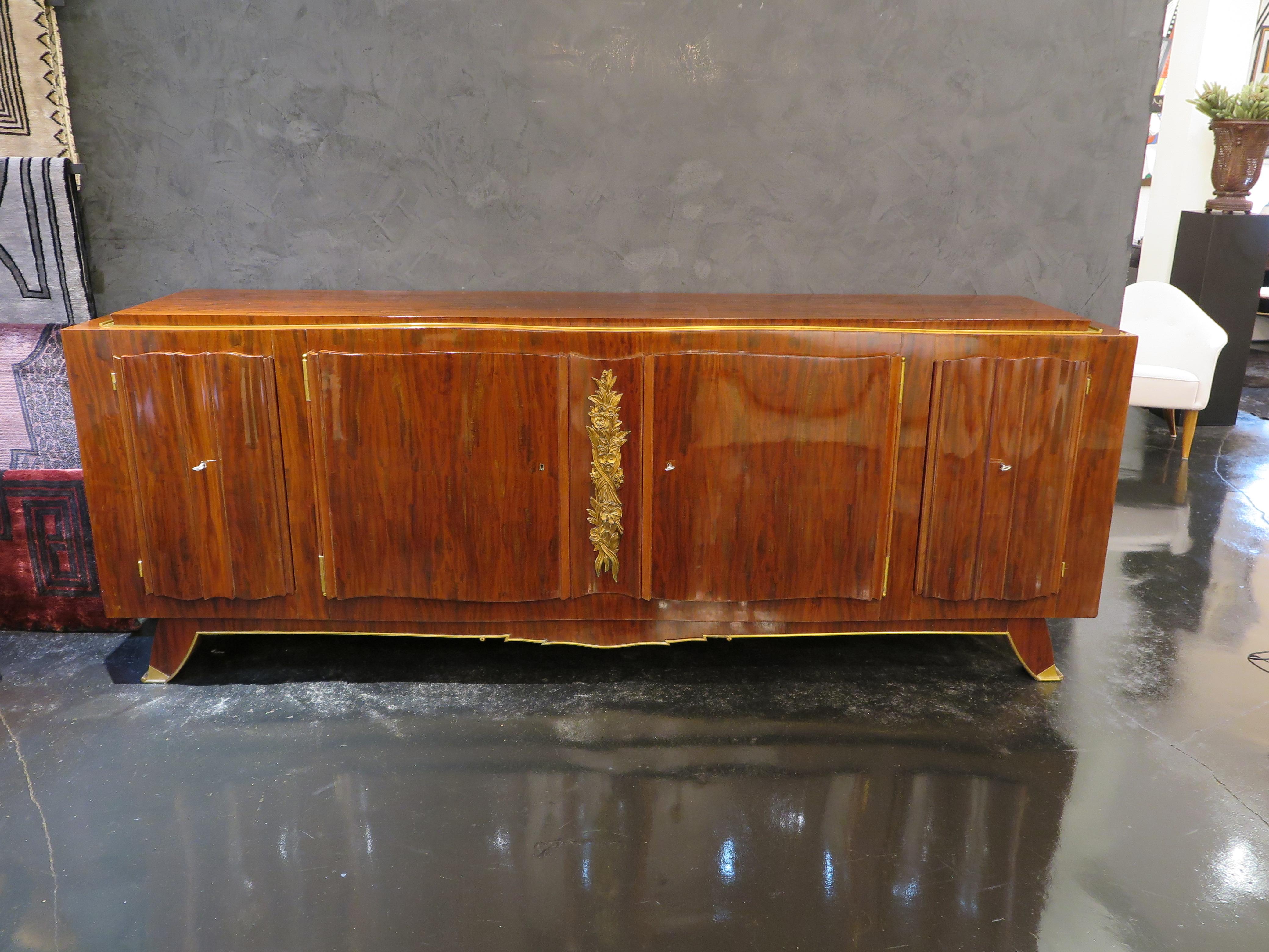 French Early 20th Century Sideboard in African Mahogany veneer. The antique Art Deco credenza features a rich floral bas-relief in gold leaf that decorates the center of the piece. The border showcases gilded details and the feet house bronze feet