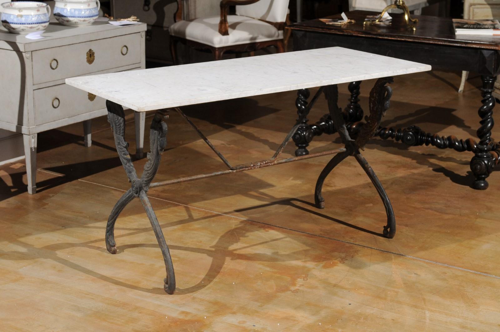 A French sofa table from the 20th century, with marble top and swan motifs. Created in France during the 20th century, this sofa table features a rectangular top sitting above an elegant iron base made of X-form legs topped with swans gracefully