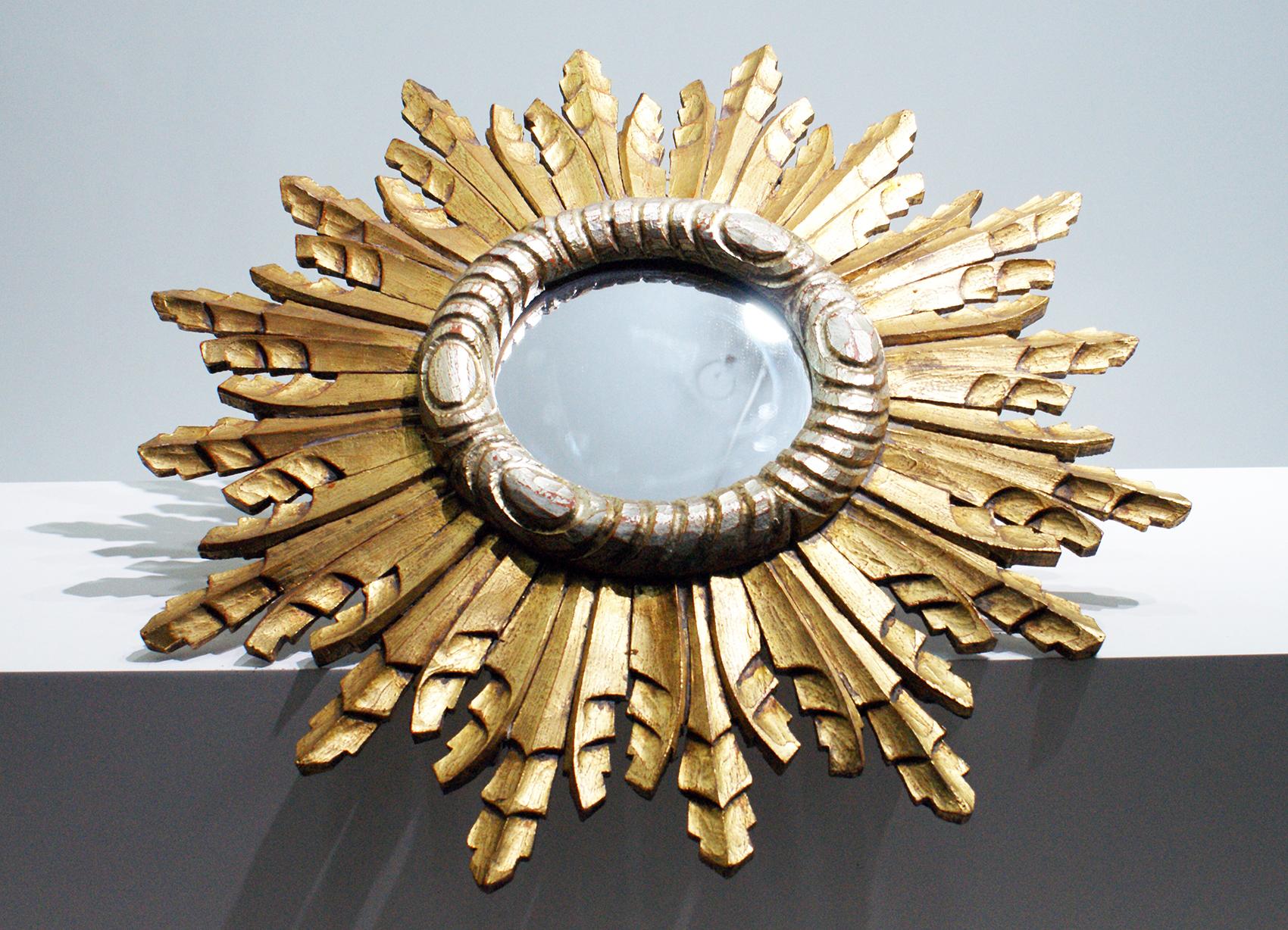 French gold sunburst mirror with carved decoration at the frame.
The mirror is surrounded by staggering lengths of silver and gilt colors sunbeams.