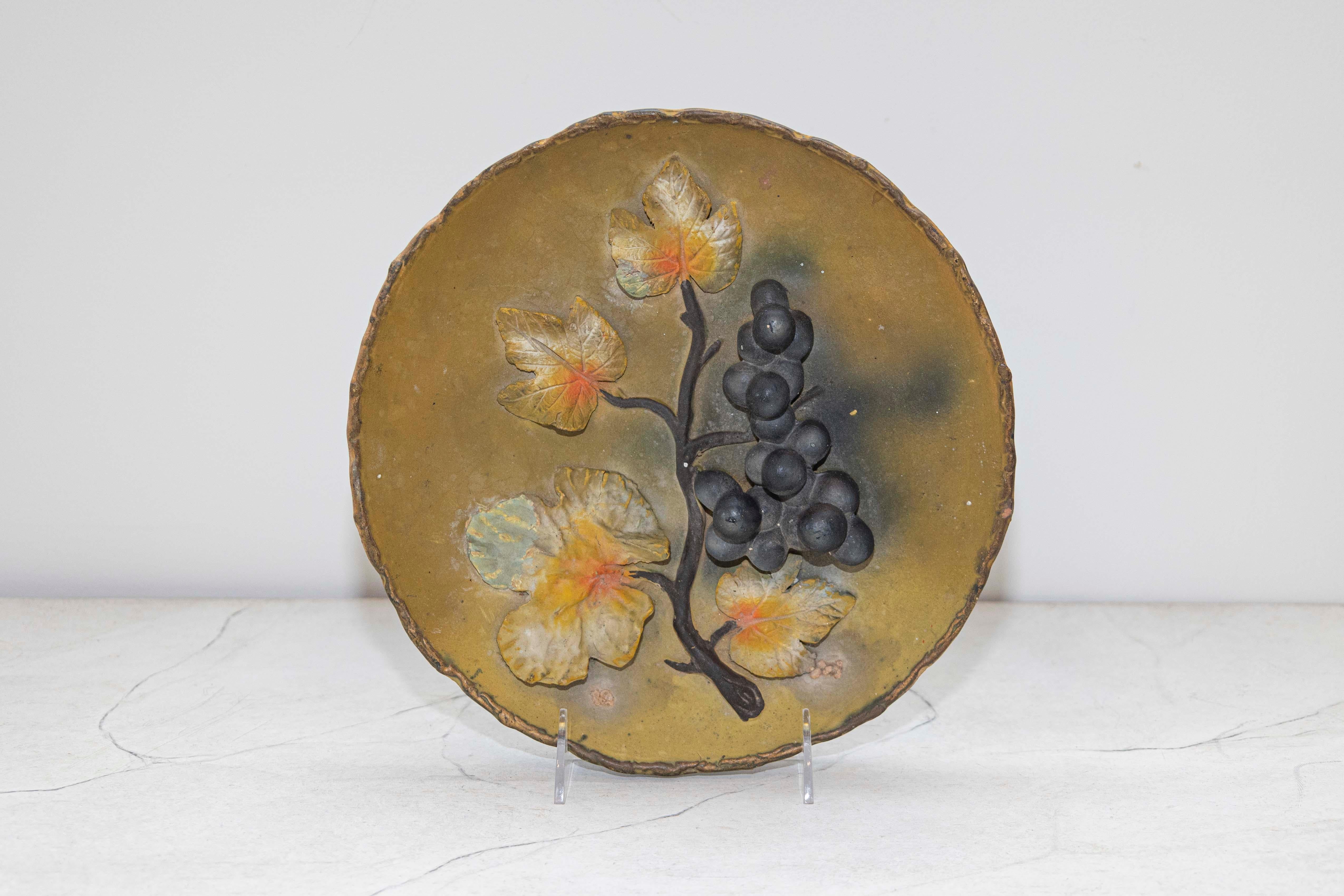 A French wall hanging pottery plate from the 20th century, with raised grape motifs. Created in France during the 20th century, this decorative plate features a mustard ground perfectly enhancing raised black grapes still connected to their branch