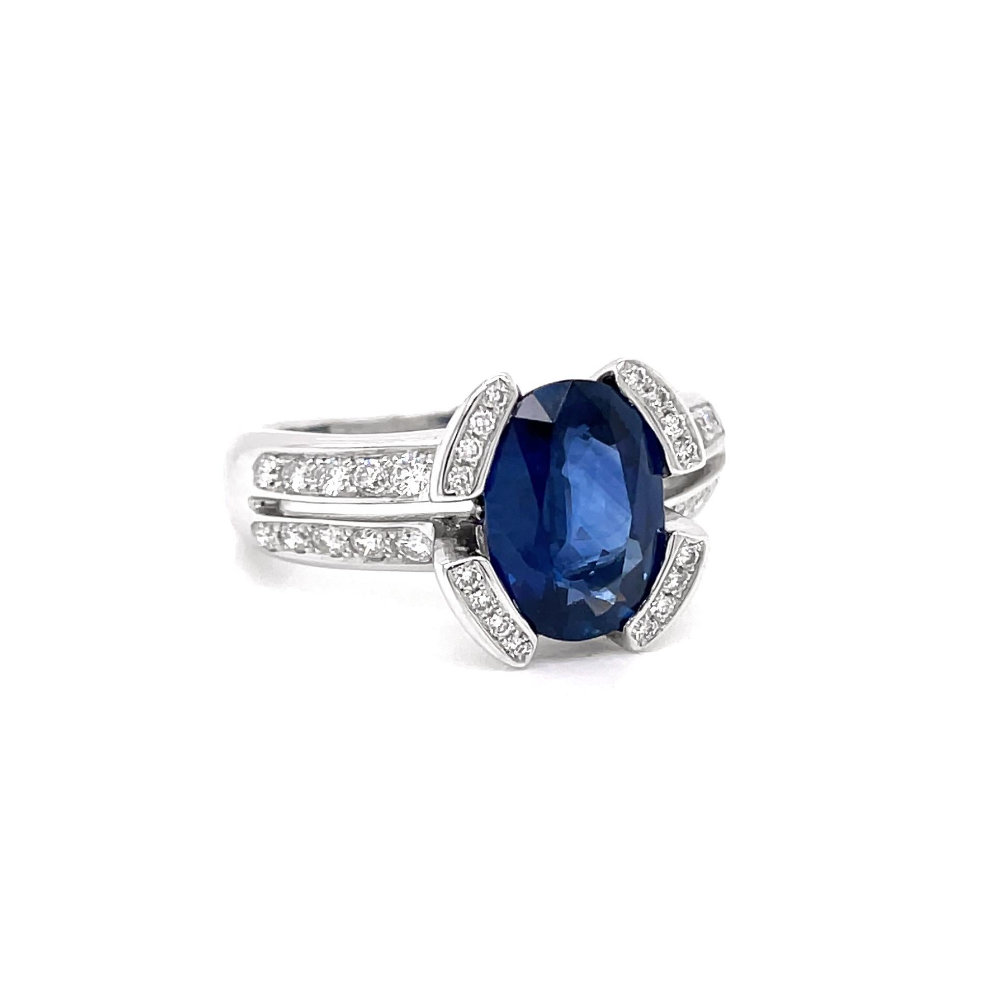 This beautiful ring features an oval 2.75ct royal blue sapphire mounted in a semi rub-over setting and split shoulder shank. The collet is split in four sections, all grain set with four round brilliant cut diamonds in each followed by a diamond