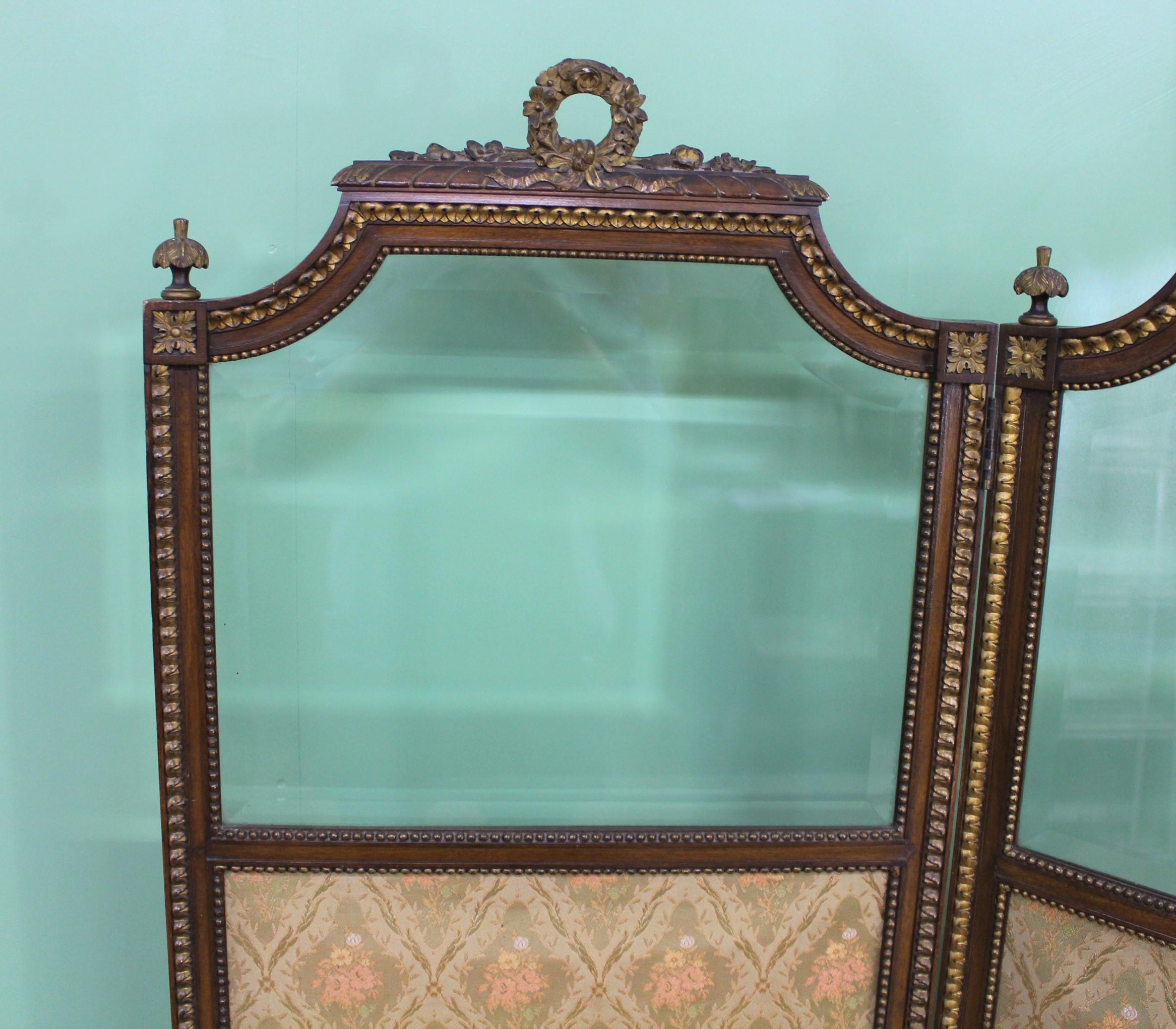 A charming and decorative French 3 fold dressing screen. Well constructed with a solid walnut frame embellished with parcel gilt decorations throughout in a neoclassical style. Fitted with its original beveled plate glass and lining material.
