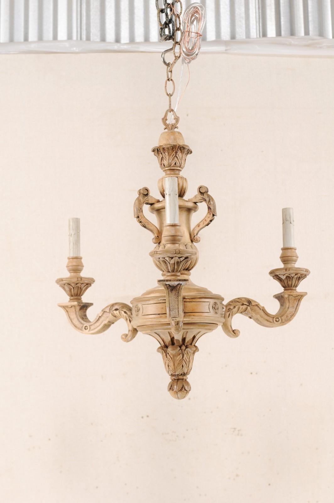 A French three-light shapely carved natural wood chandelier from the mid-20th century. This vintage chandelier from France features an ornately decorated central gallery with an urn-shaped carving, with pierced handles, atop the more bulbous mid