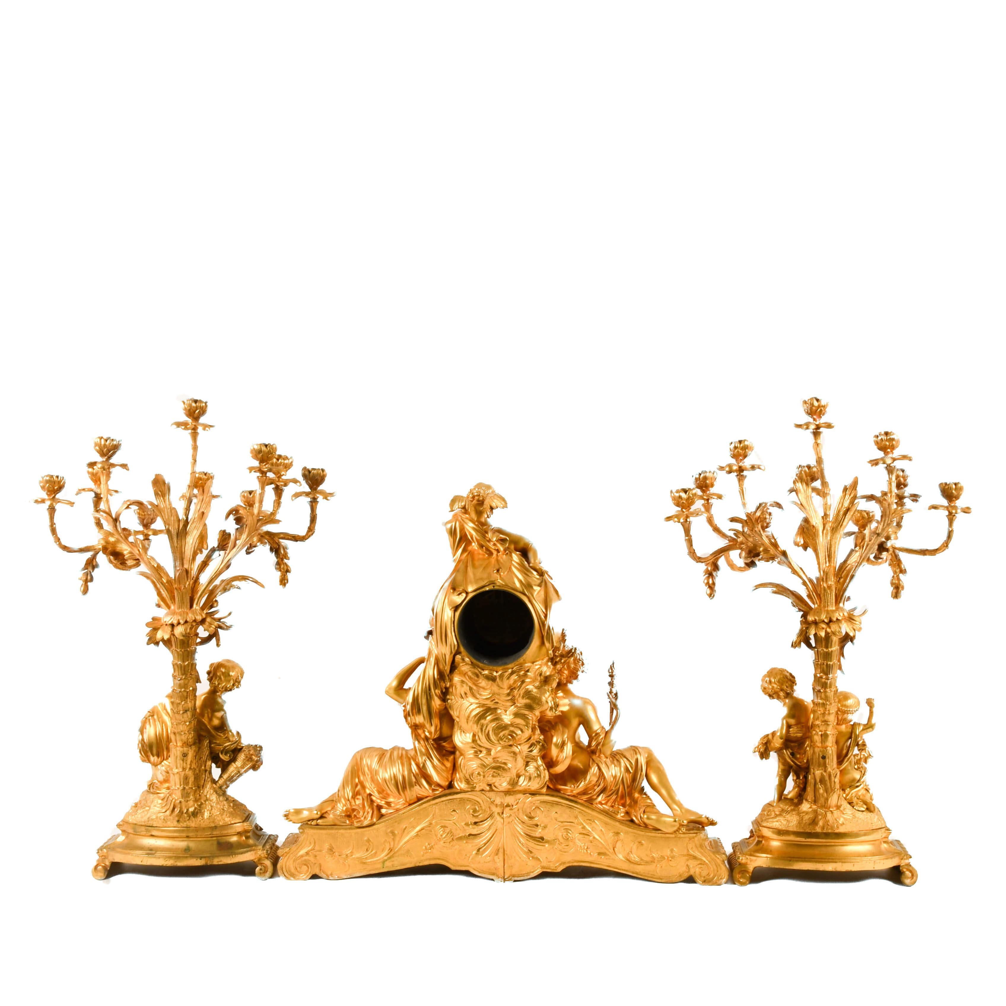 Step into the lavish splendor of French high design with this Antique Three-Piece Palatial Dore Bronze Garniture Clock Set. A triumph of opulence and artisan mastery. Dripping in radiant gilt bronze, this ensemble commands attention with its