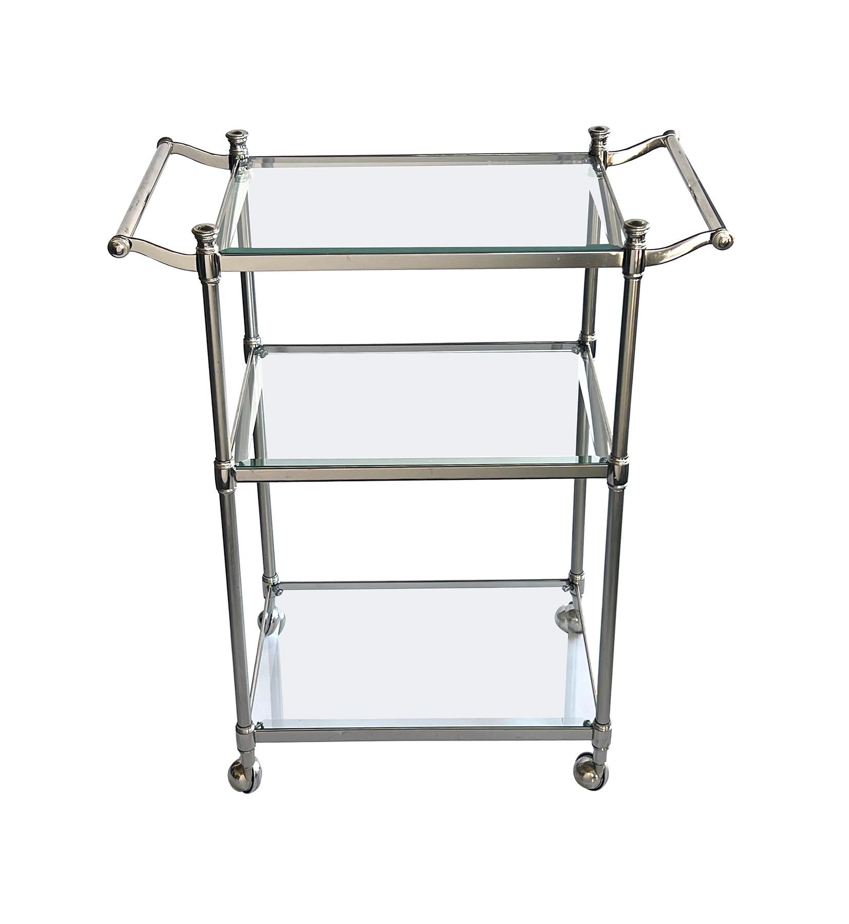 Idéale pour les petits espaces, elle est fabriquée en chrome poli et brossé et supporte trois étagères en verre biseauté reliées par des supports en forme de colonne, le tout flanqué de poignées à volutes et monté sur des roulettes en acier.