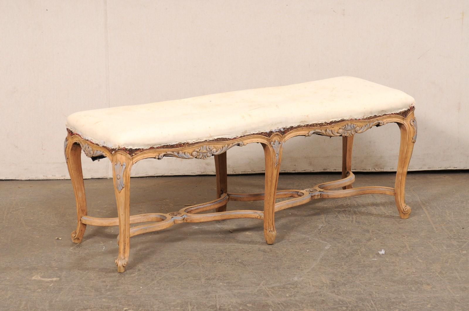 A French nicely-carved wood bench with upholstered seat, from the mid 20th century. This vintage backless bench from France has an upholstered seat, set within a carved wood frame with a gracefully scalloped skirting on all sides, adorn with foliate