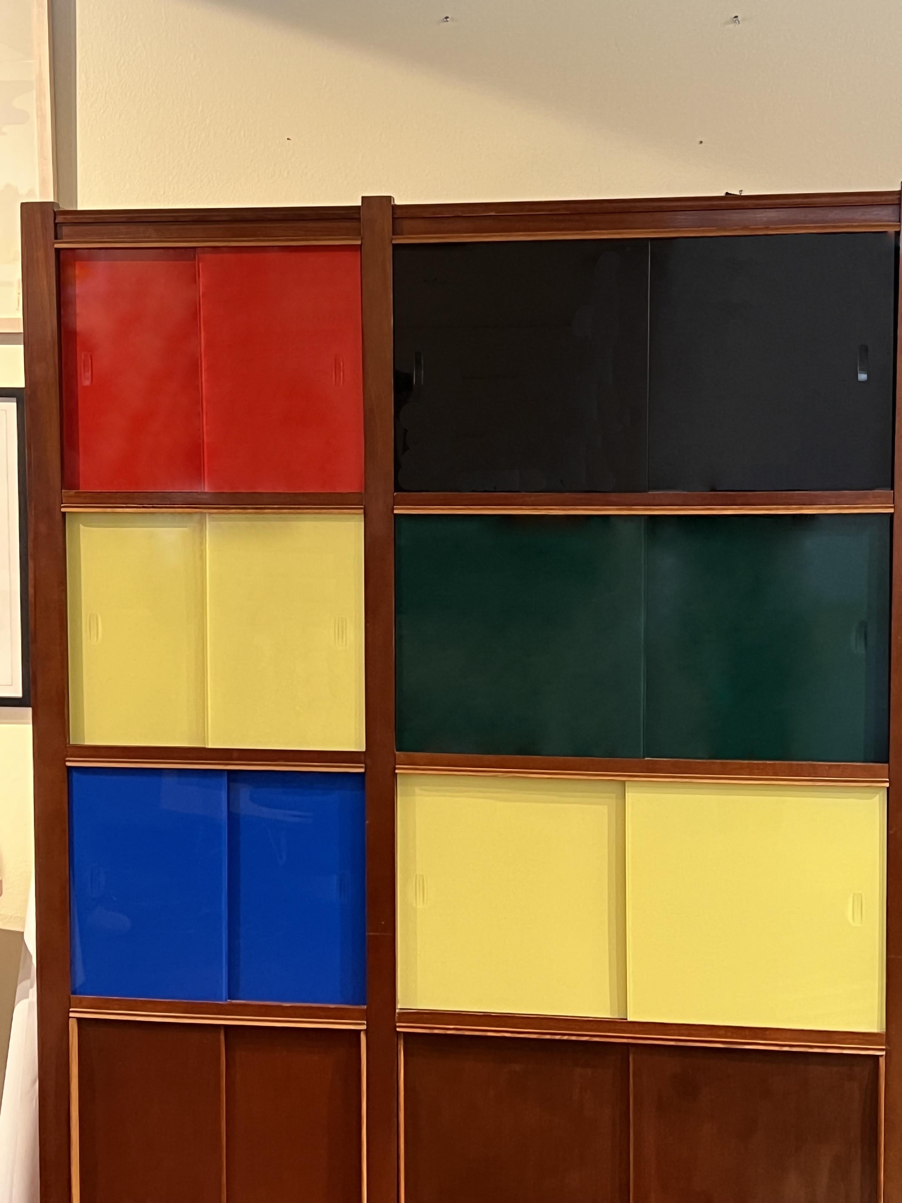 Outstanding 1950s mahogany bookcase featuring 12 cubicle parts. The sliding doors on the bottom are in mahogany whereas the other ones are in red, yellow, blue, black, and green glass reminding us Charlotte Perriand and Jean Prouve bookshelves.