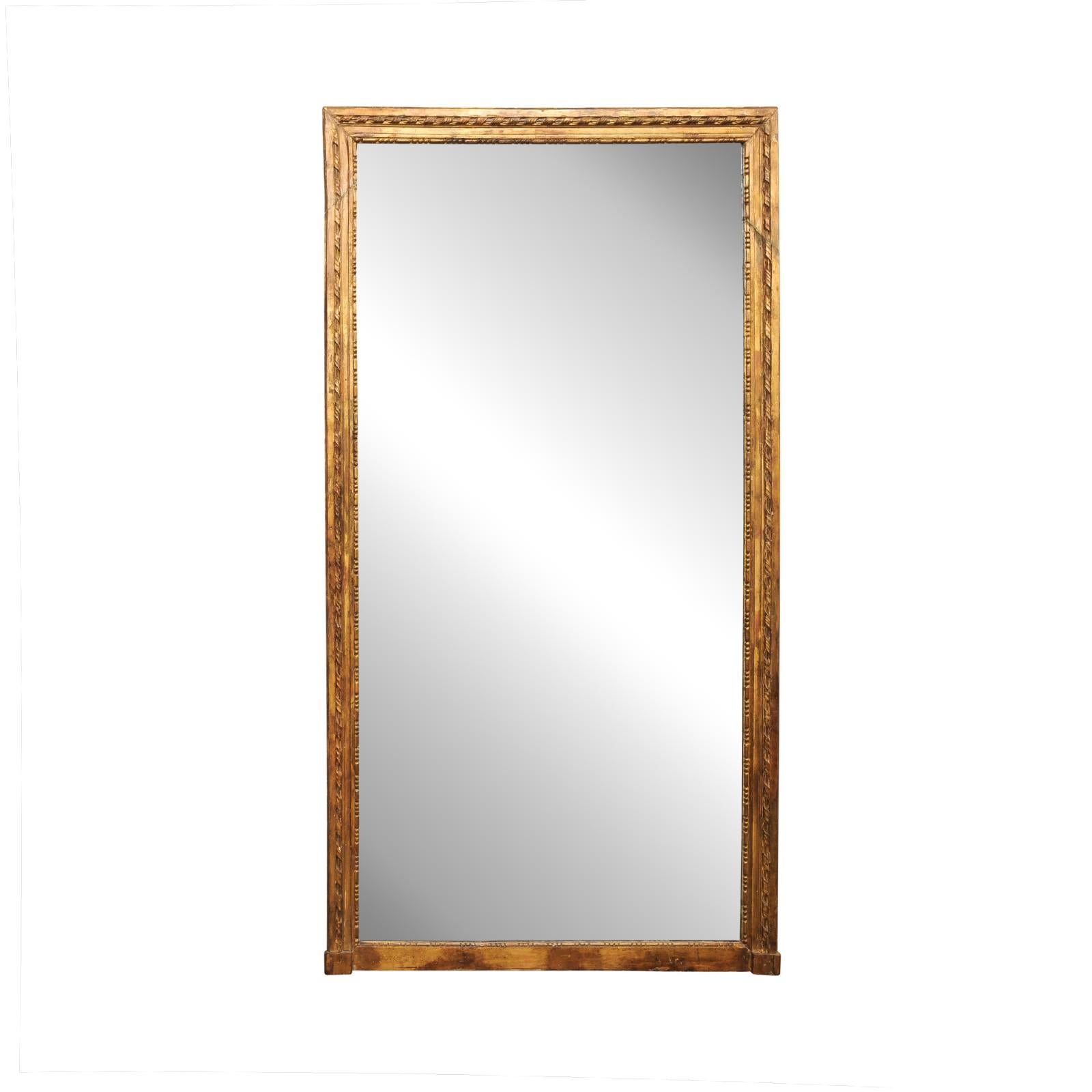 Un alto espejo de pared francés de tonos dorados con grandes adornos del siglo XIX. Este espejo antiguo de Francia tiene una robusta forma rectangular y está diseñado con líneas limpias en el borde exterior, y una moldura bellamente estratificada en