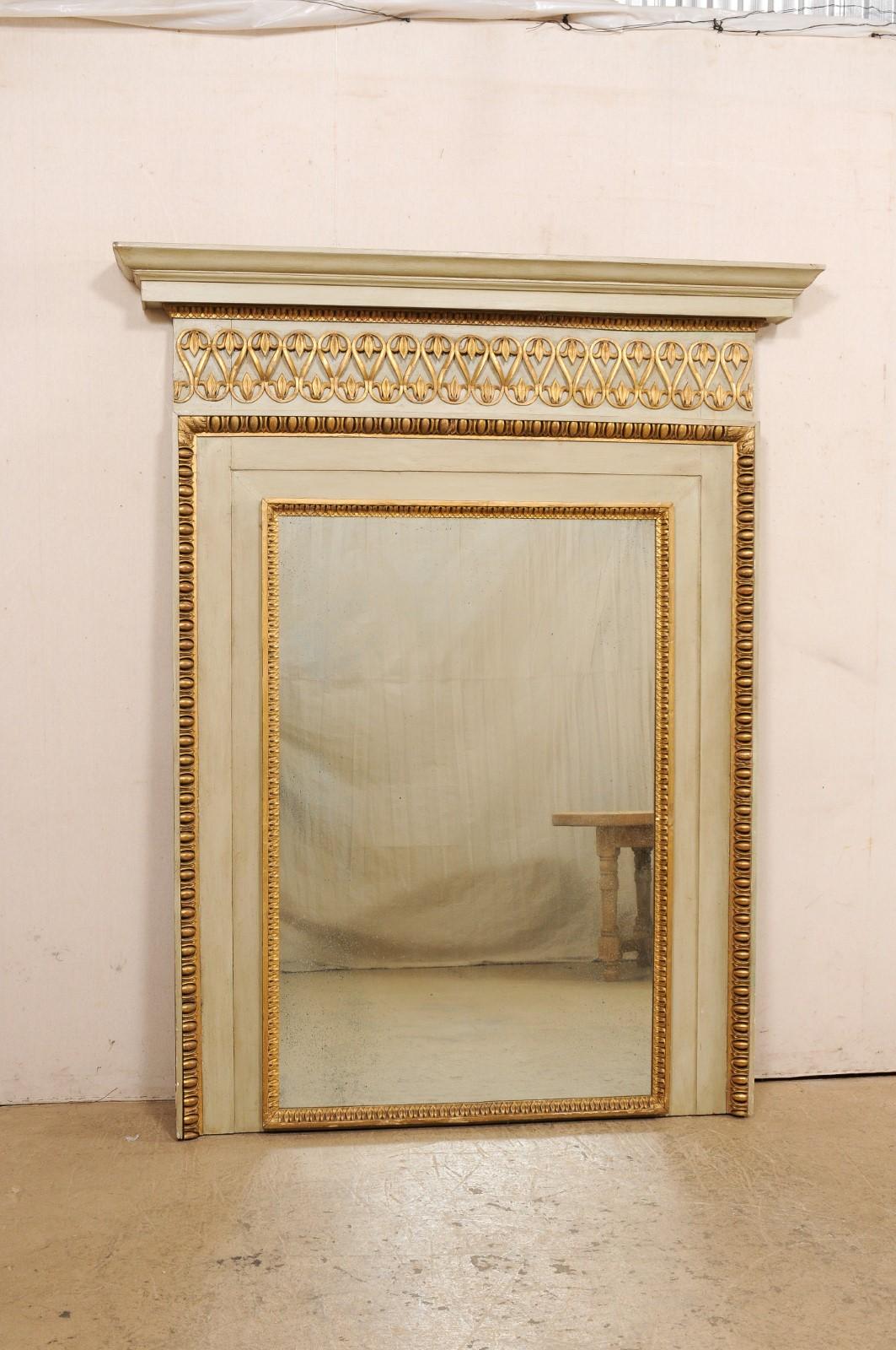 A French painted and carved wood trumeau-style mirror from the mid 20th century. This mid-century mirror from France, has a vertical-rectangular shape, and features a nicely molded upper cornice, elegant trimmings in gilt with a undulating pattern