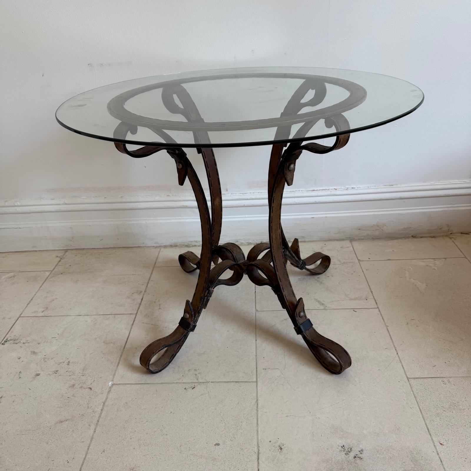 Una elegante mesa de centro circular de metal con acabado patinado cobrizo, base creada como si estuviera hecha de correas y hebillas de arnés de cuero. Con reminiscencias de los diseños de Hermes, resultará llamativo en un ambiente de sastrería.