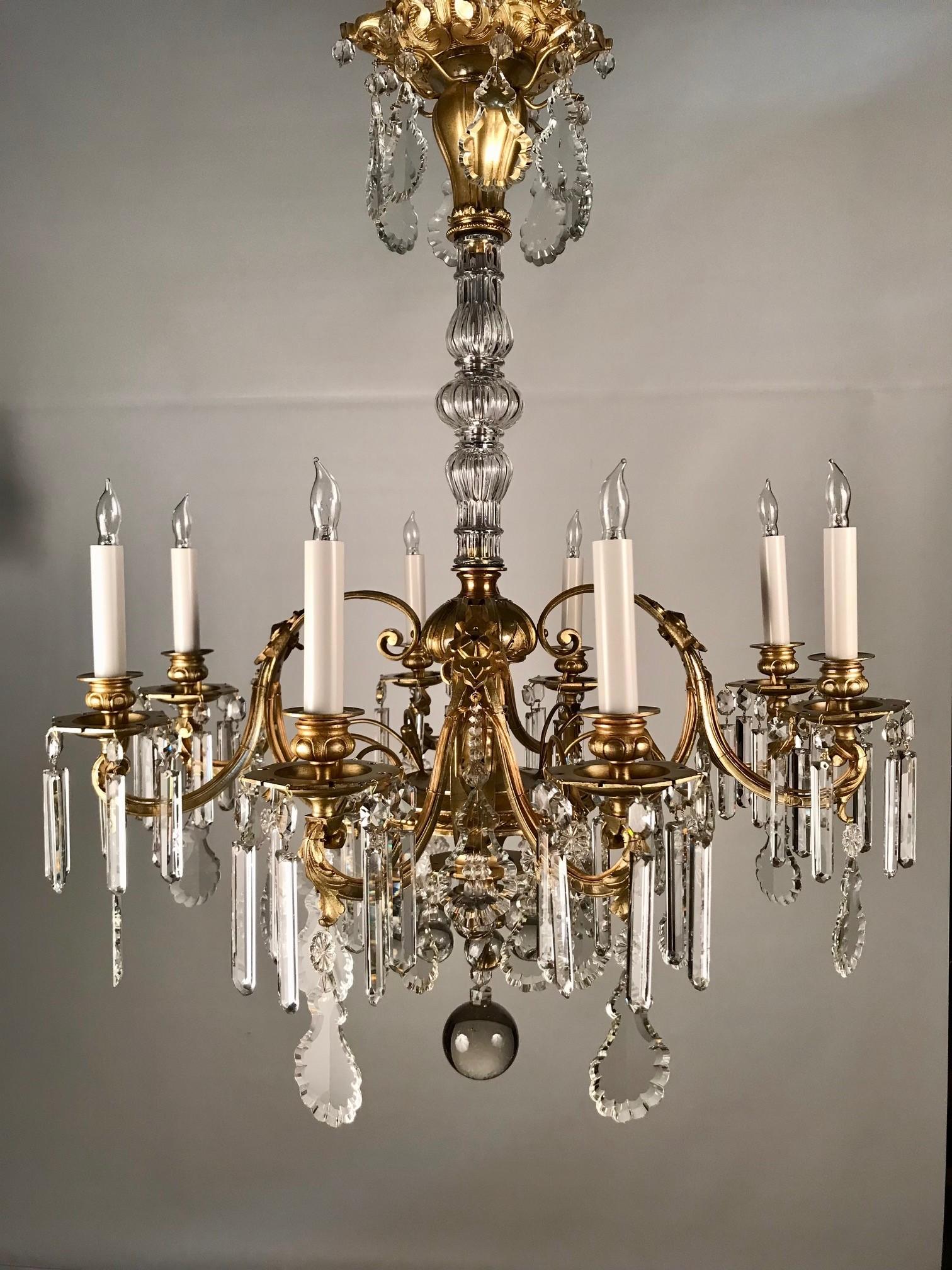 This elegant Louis XV style chandelier has scrolling arms applied with acanthus and mounted on a bronze central body. Unusually this has flower form short stems, from which are hung further cut ornaments. The central stem is sheathed in