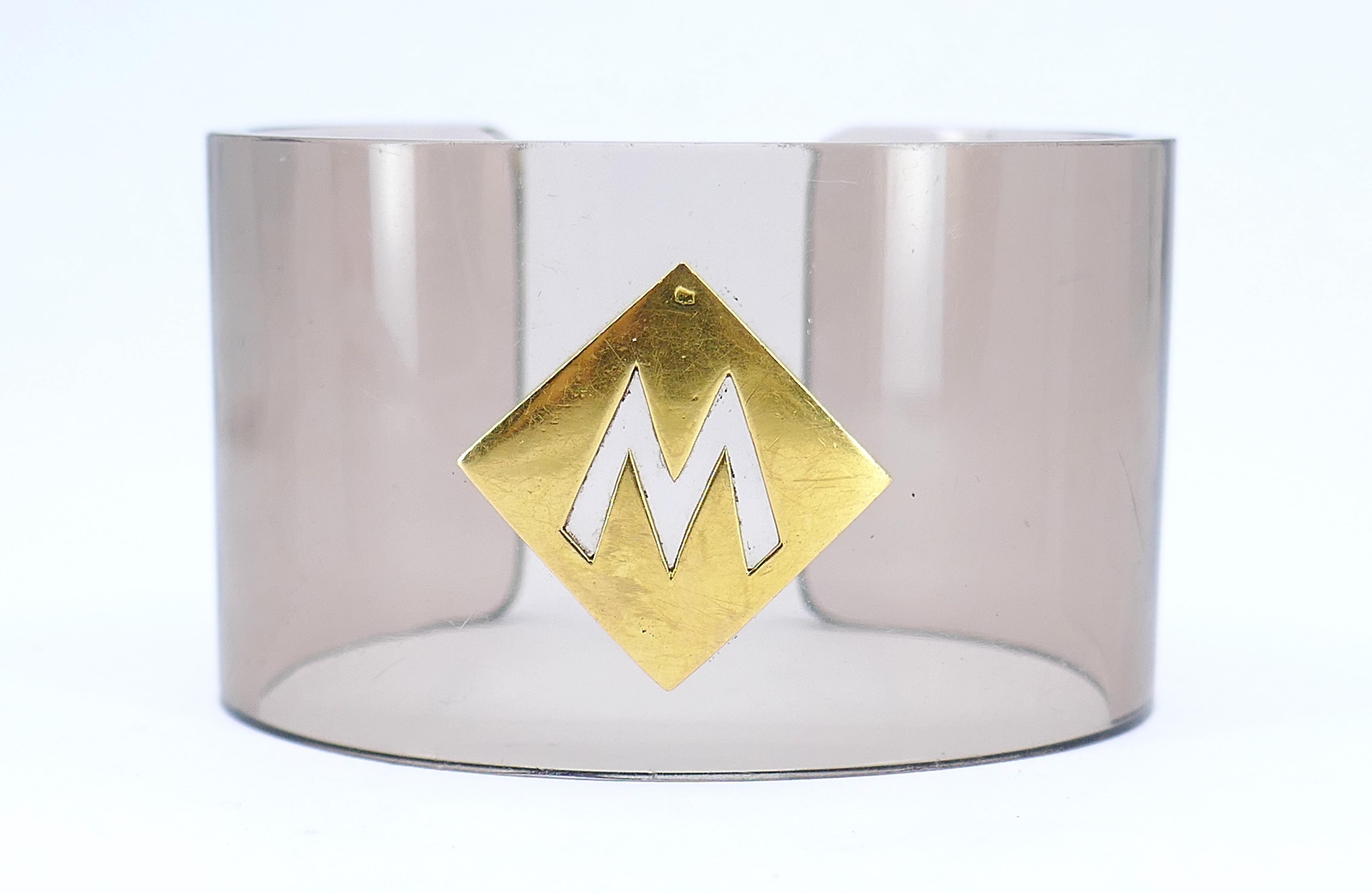 This French acrylic cuff seamlessly merges modern design with timeless elegance. Adorned with an 18K gold rhombus, the striking cutout in the shape of the letter 'M' adds a personalized touch. With an inner circumference of 6