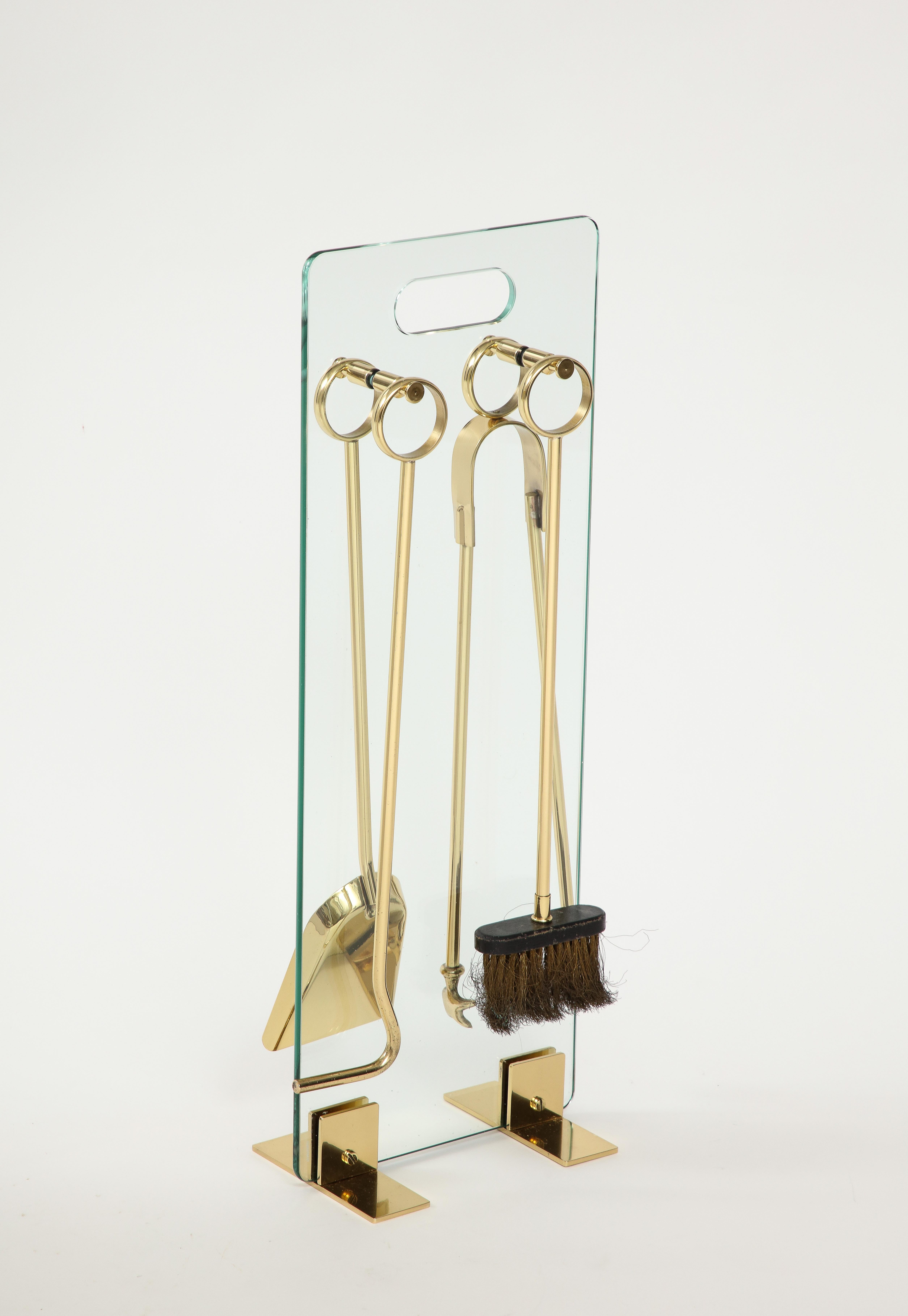 French Modernist set of brass fire tools suspended on a glass frame, in the style of Jacques Adnet. Professionally polished.