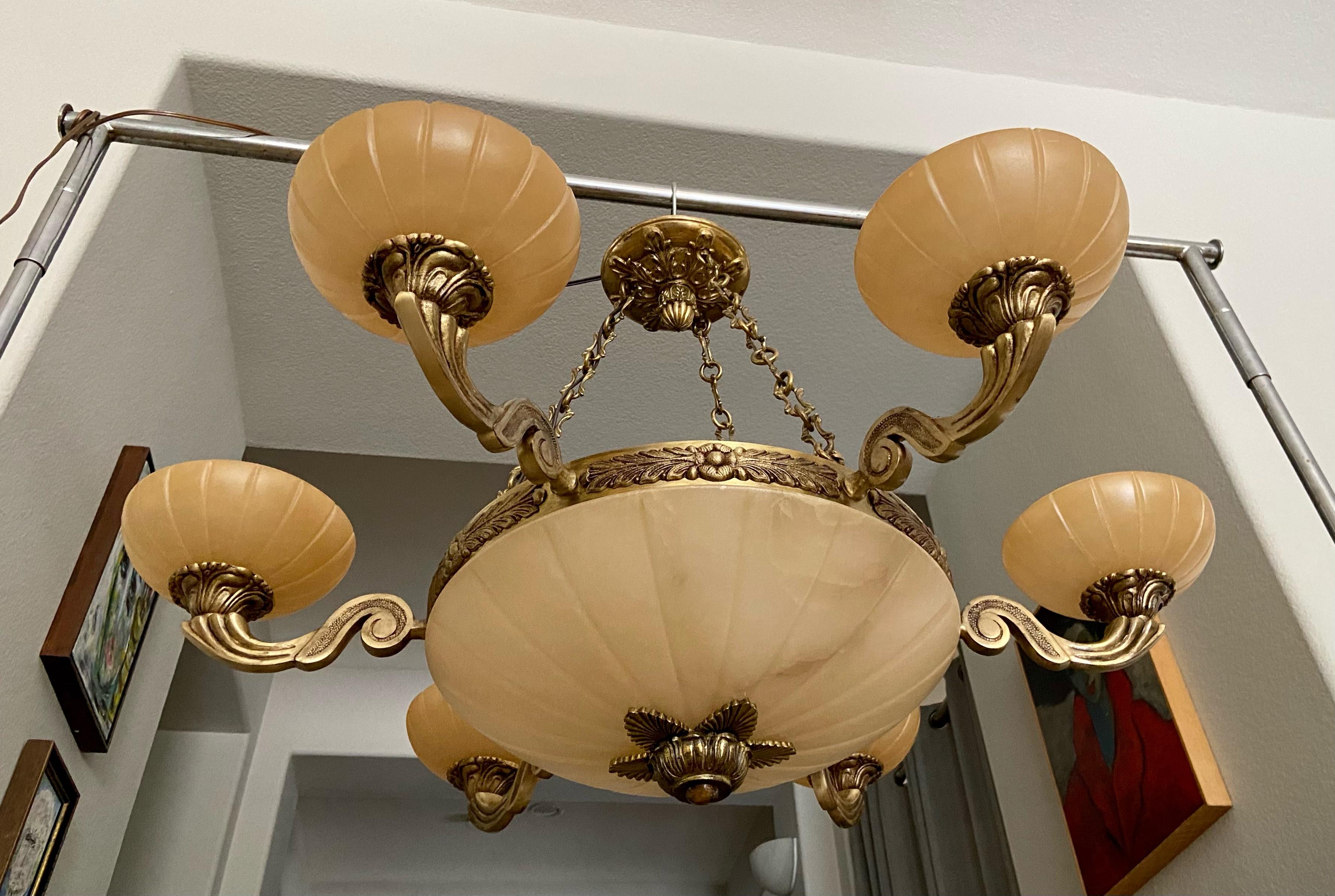 French style alabaster 6 arm chandelier with brass fittings, chain and ceiling cap. The alabaster stone is pale tan with nice veining detailing. Fixture uses 9 candelabra B base bulbs (3 main large bowl, one each 6 arms). Overall diameter 35