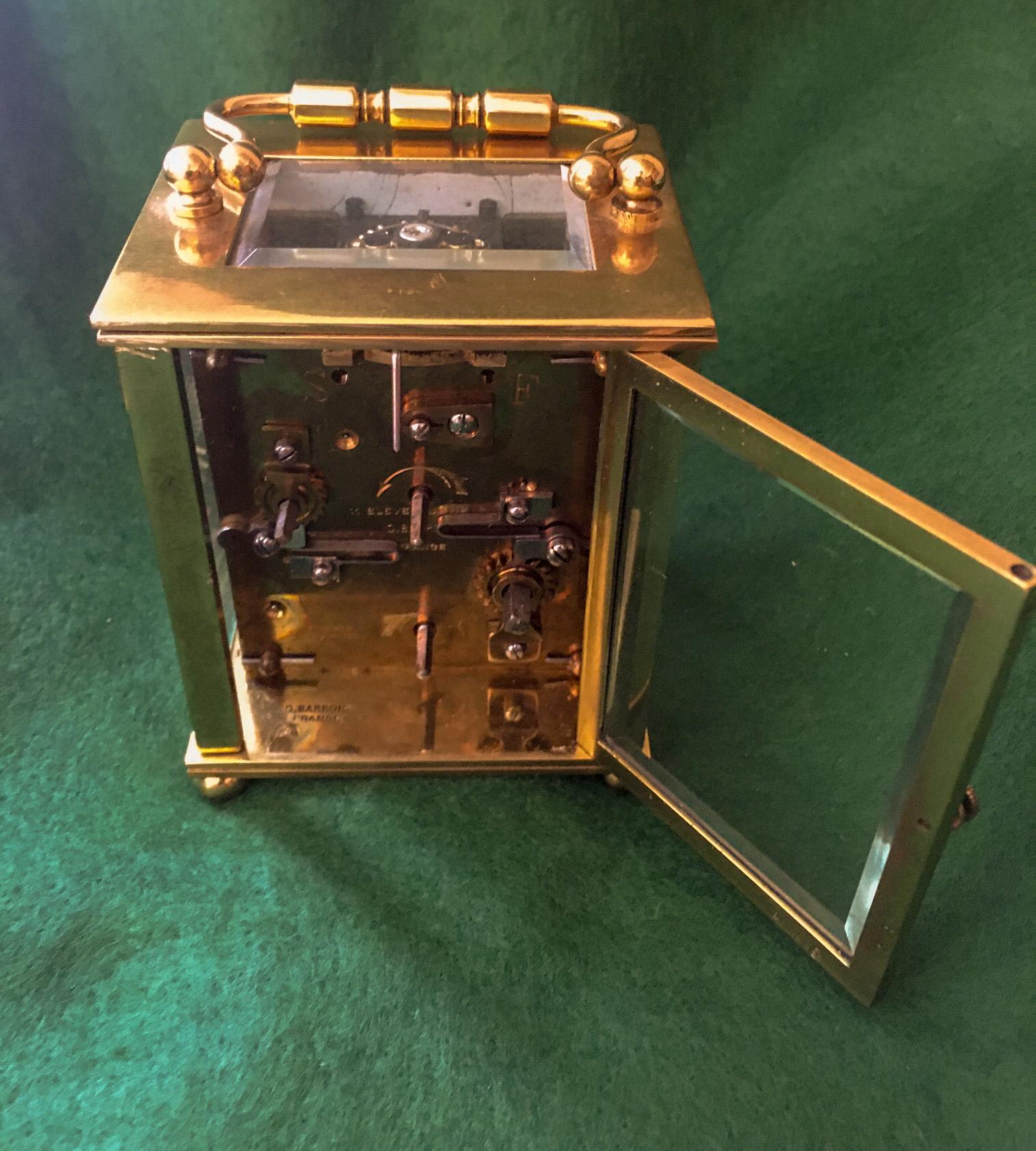 This classic French alarm carriage clock was made by Delépine-Barrois and features a  brass Cubique shaped case with rectangular
top with folding handle over a beveled glass escapement
aperture with four beveled glass sides held by plain
columns and