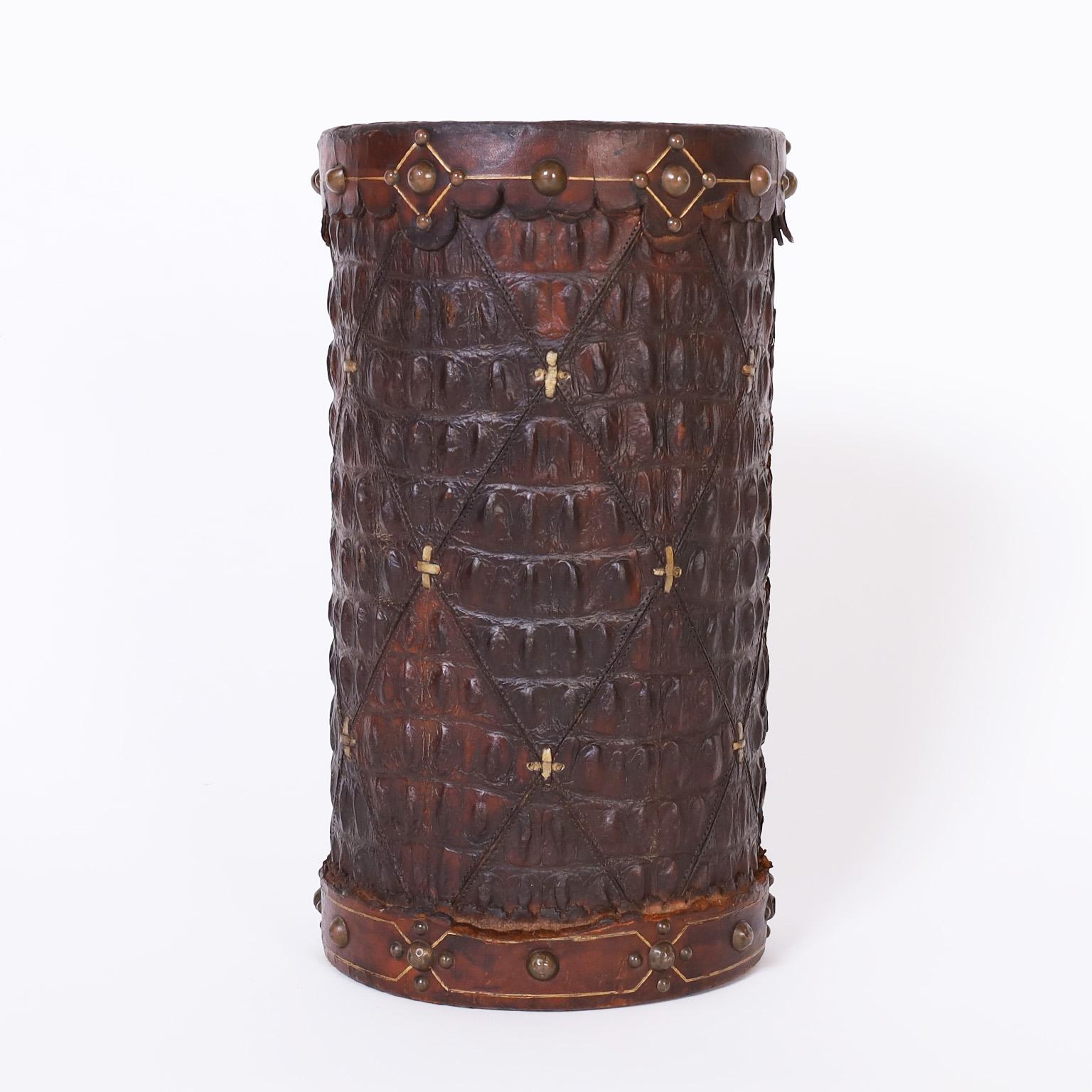For the person who has everything, an antique trash bin clad in alligator stitched in a diamond pattern with a tooled leather top and bottom cuff decorated with brass tacks.