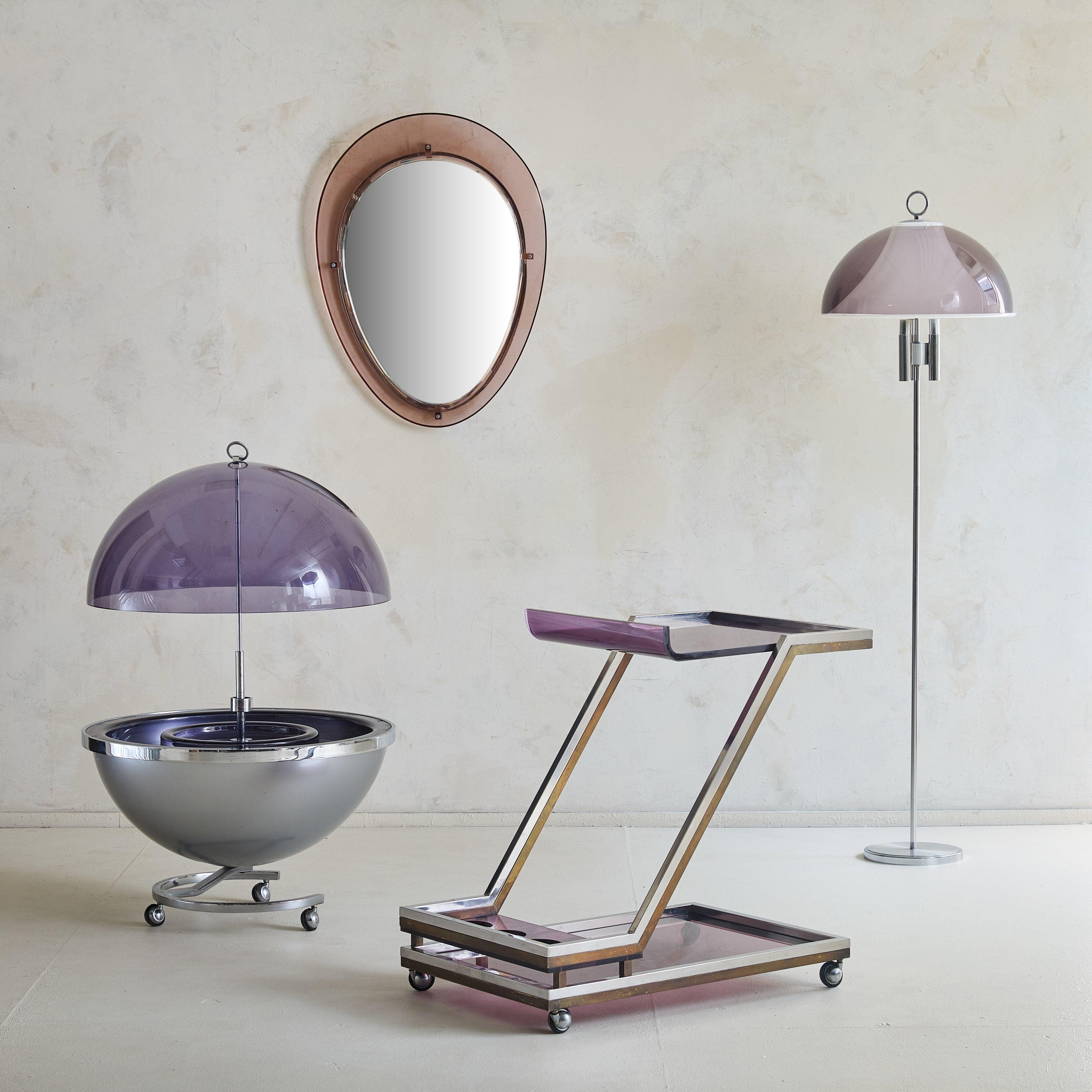 A sculptural 1970s French bar cart in the manner of Michel Dumas. The 3-tier, Z-shaped silhouette is crafted from chrome and brass, with rich amethyst smoked plexiglass surfaces. The middle tier features four integrated bottle holders, while castors