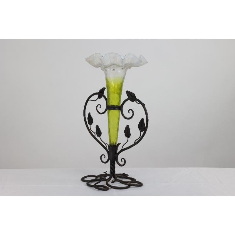 An Art Nouveau French epergne with an organic hand-made iron frame holding a glass flower vase with a green colored stem that flows into Vaseline through to the frilly top.
