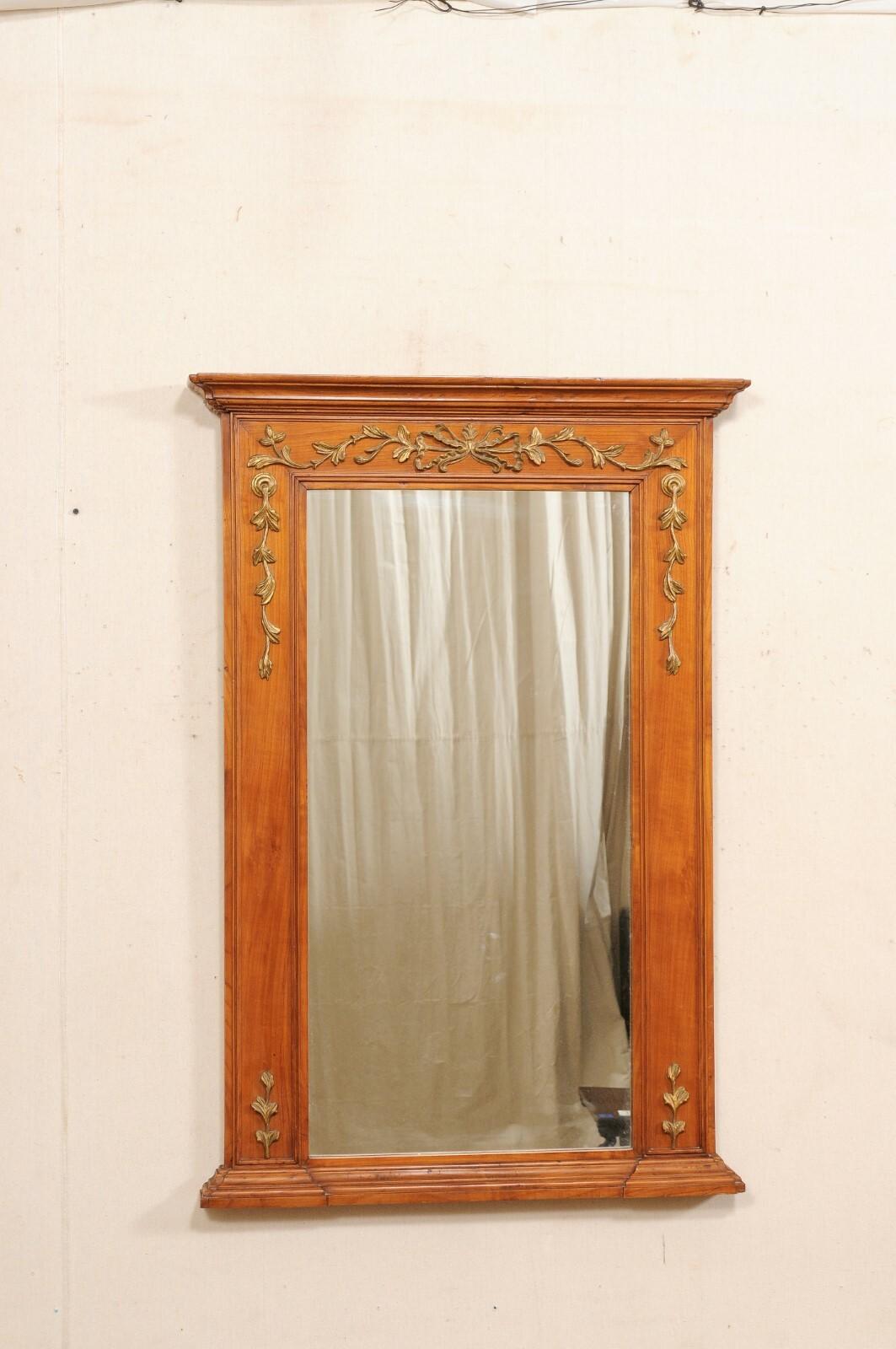 A French over-mantle carved-wood mirror from the early 20th century. This antique mirror from France stands approximately 4 feet in height. It is rectangular in shape with a nicely molded top cornice, and floral garland embellishments with a bow-tie