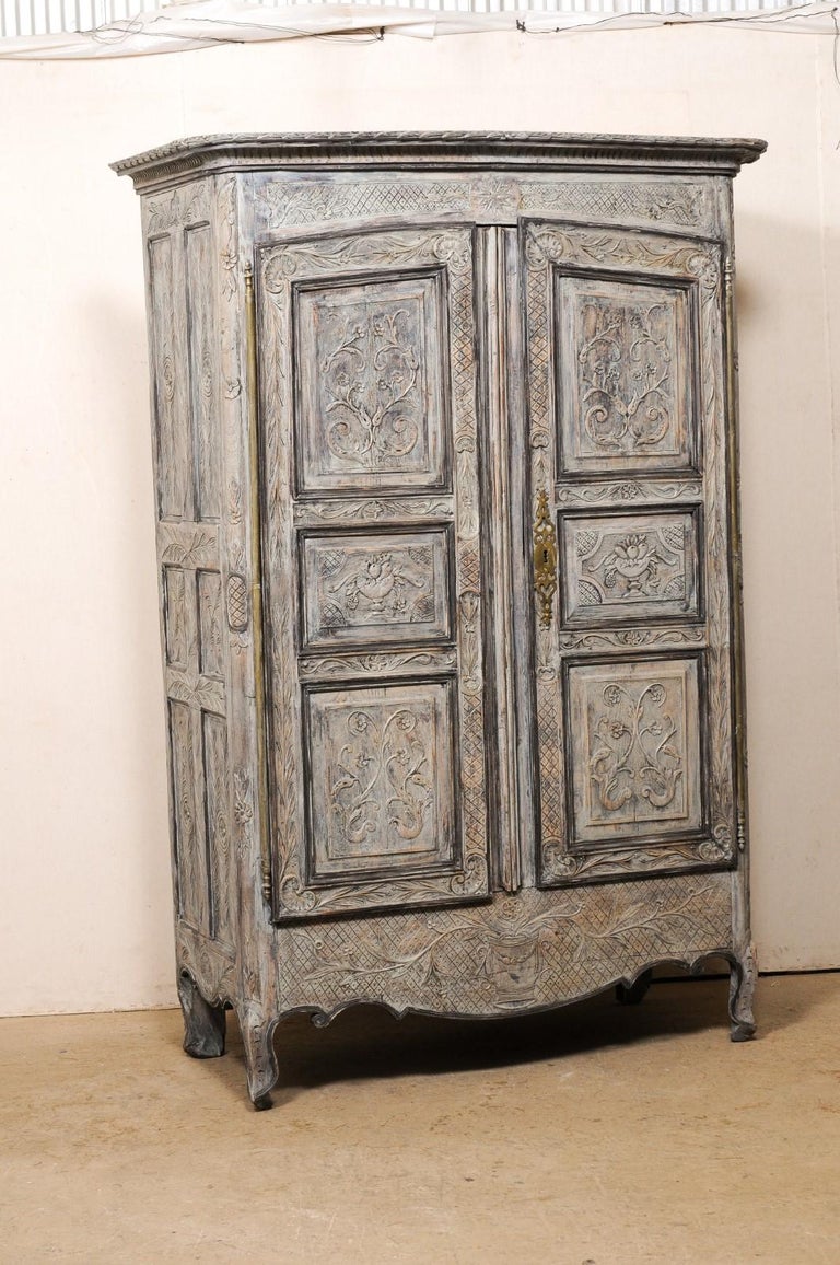 A French tall two-door cabinet with intricate carvings from the turn of the 18th and 19th century. This antique wooden armoire from France has been beautifully and ornately adorn throughout with hand-carved neoclassical embellishments in a foliage